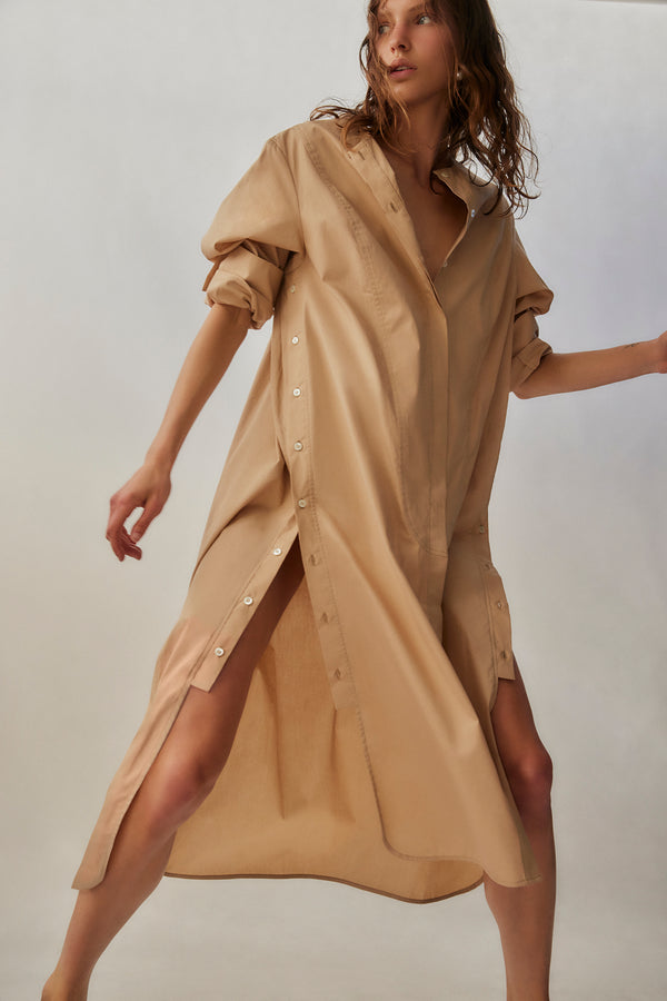 Woman wearing a beige button-up dress against a plain background