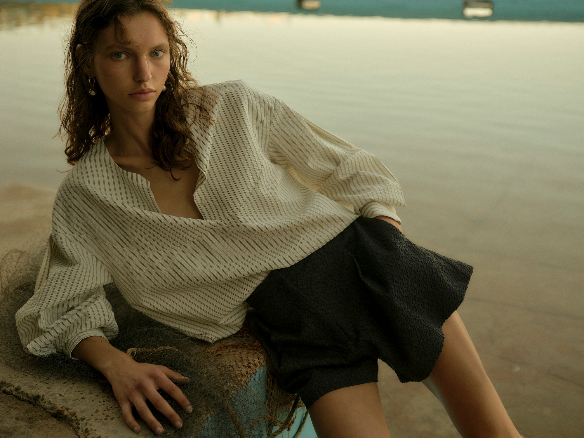 Woman wearing a white blouse with puffed sleeves and dark shorts against a textured wall.