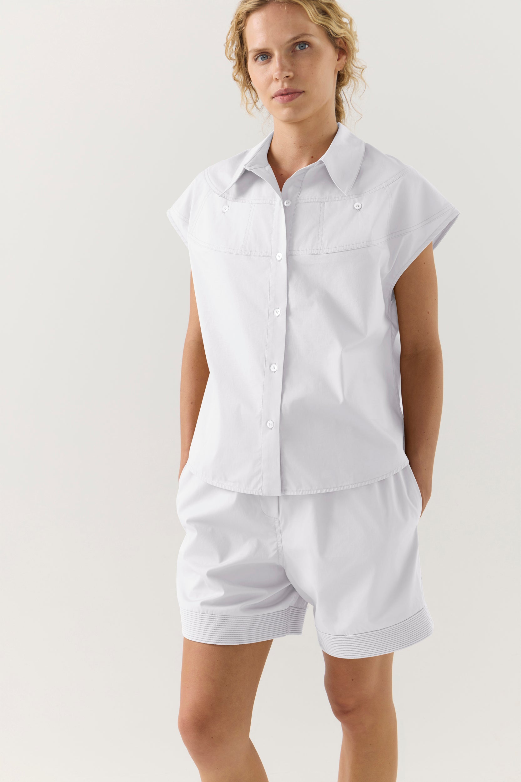 Woman wearing a white sleeveless shirt and shorts on a plain background
