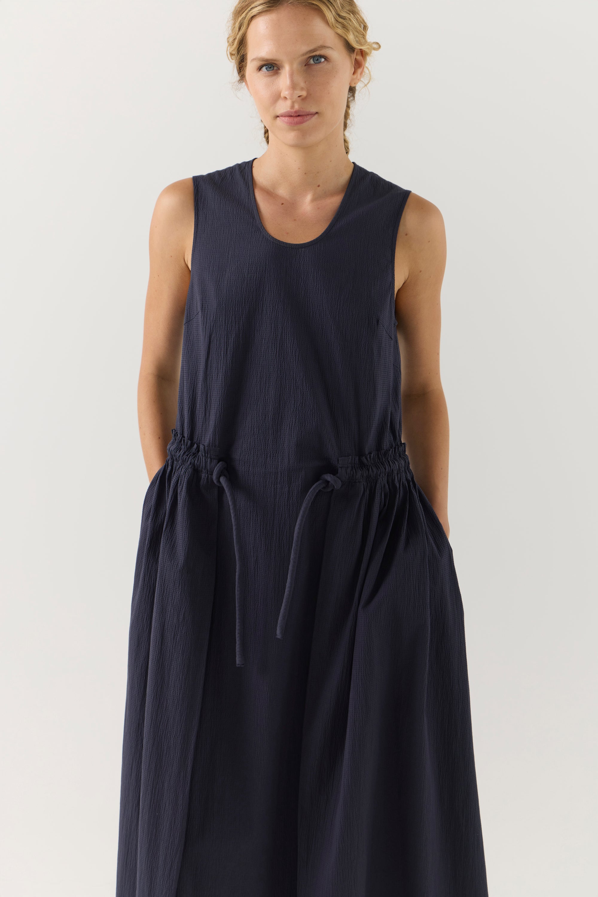 Woman wearing a sleeveless navy dress against a white background