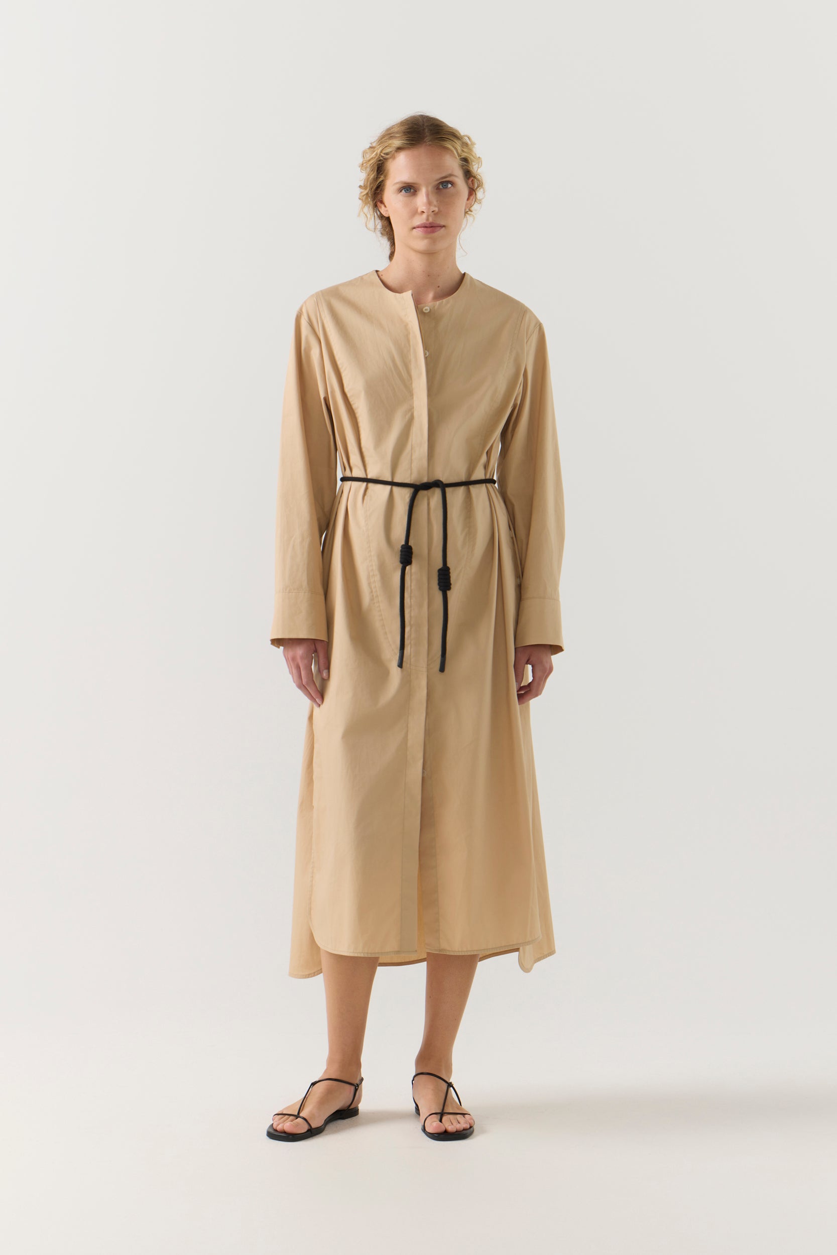 Woman wearing a beige dress with a belt on a white background