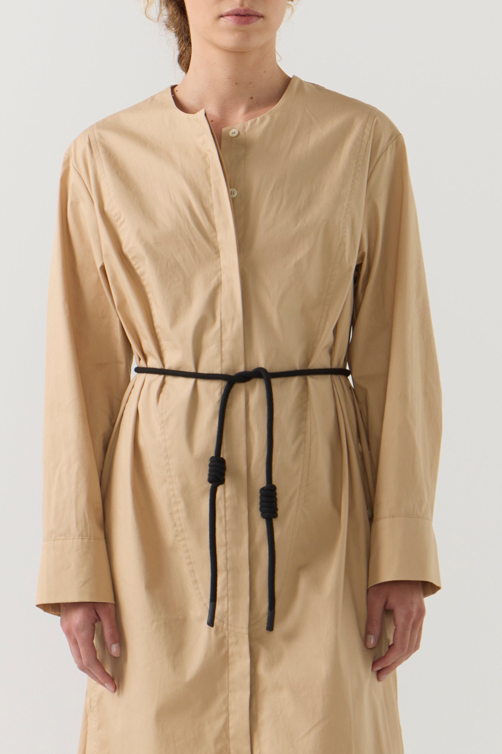 Person wearing a beige long-sleeve dress with a black belt on a white background