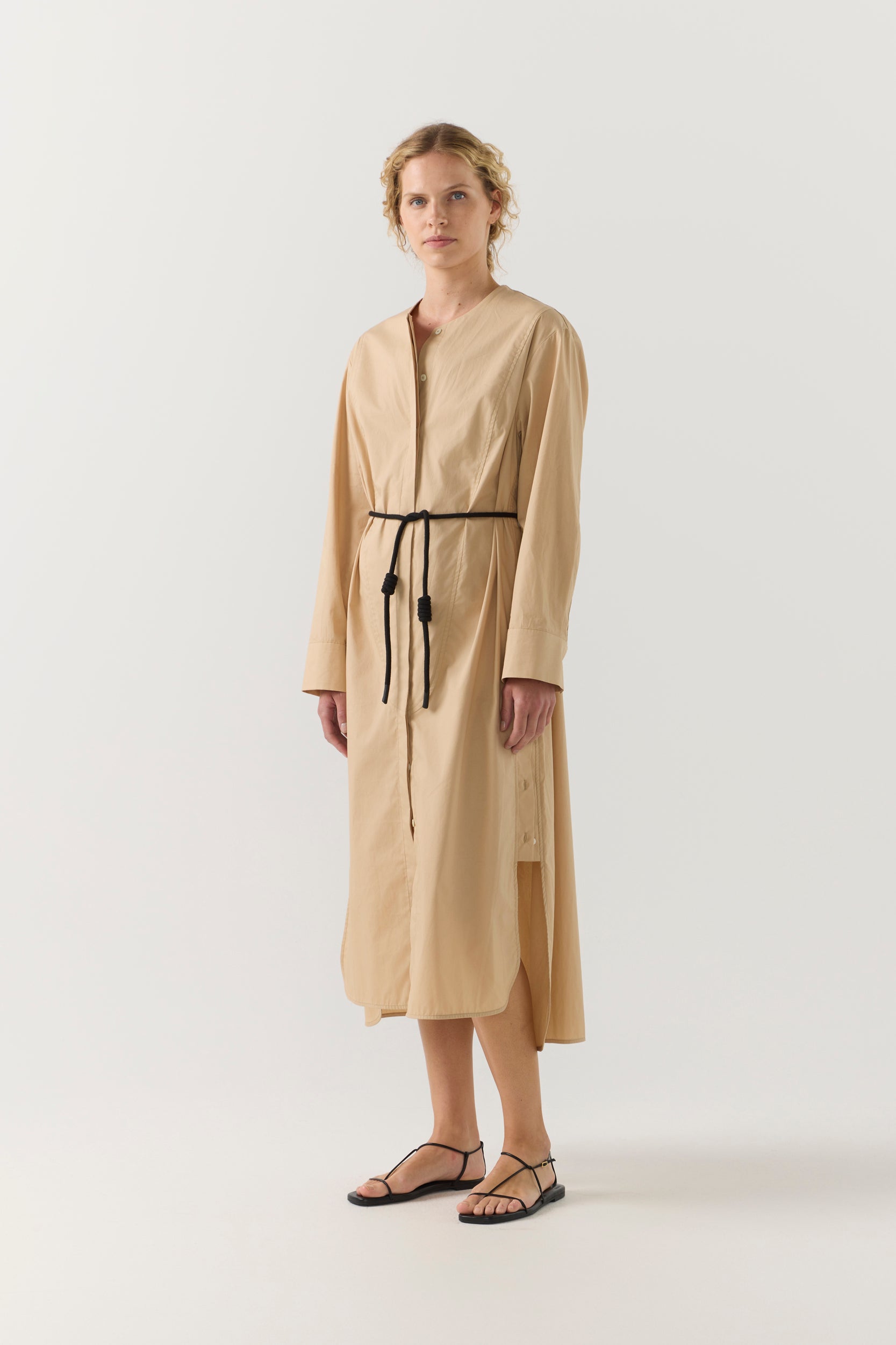 Woman wearing a beige dress with a belt on a white background