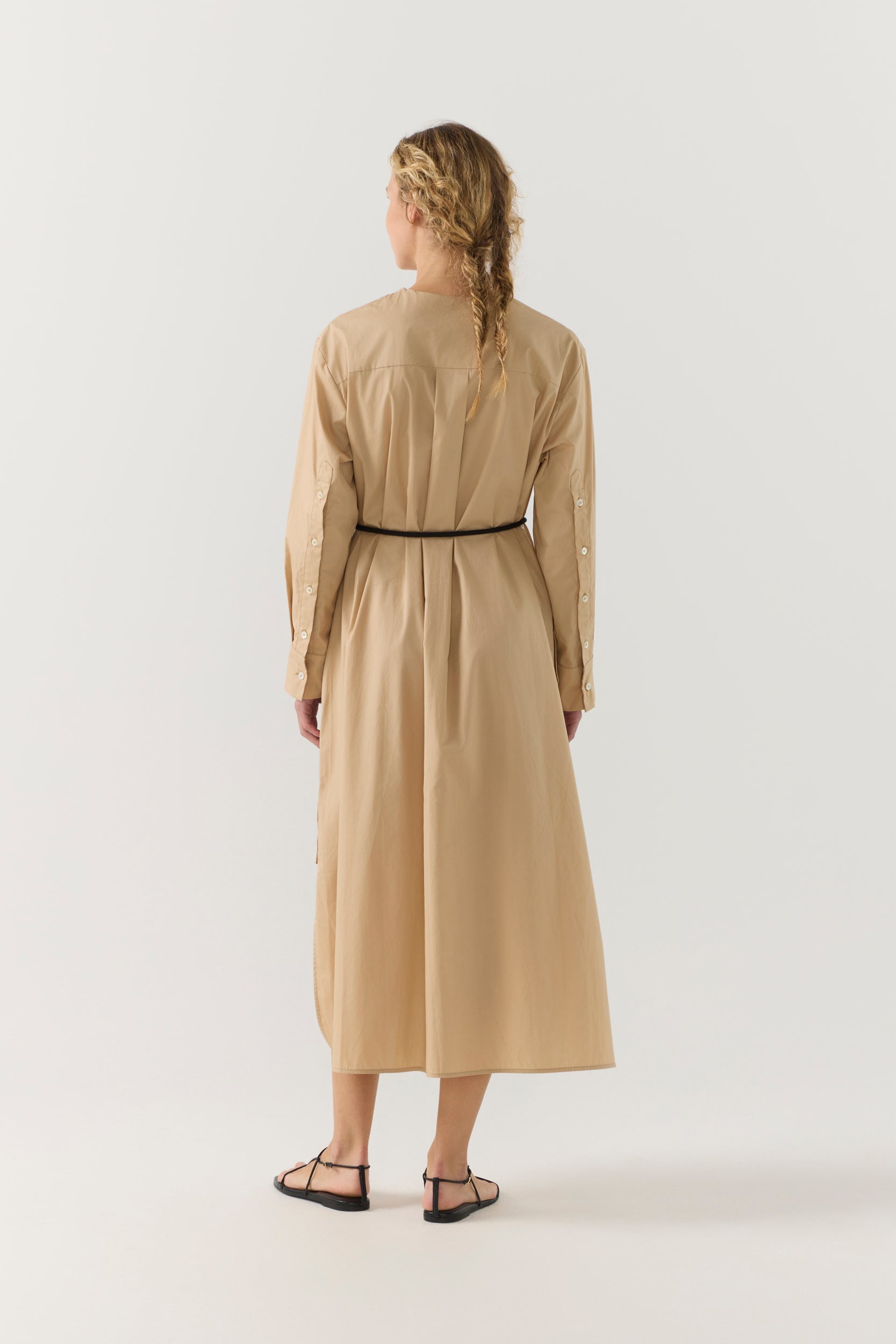 Woman wearing a beige dress with a belt on a white background