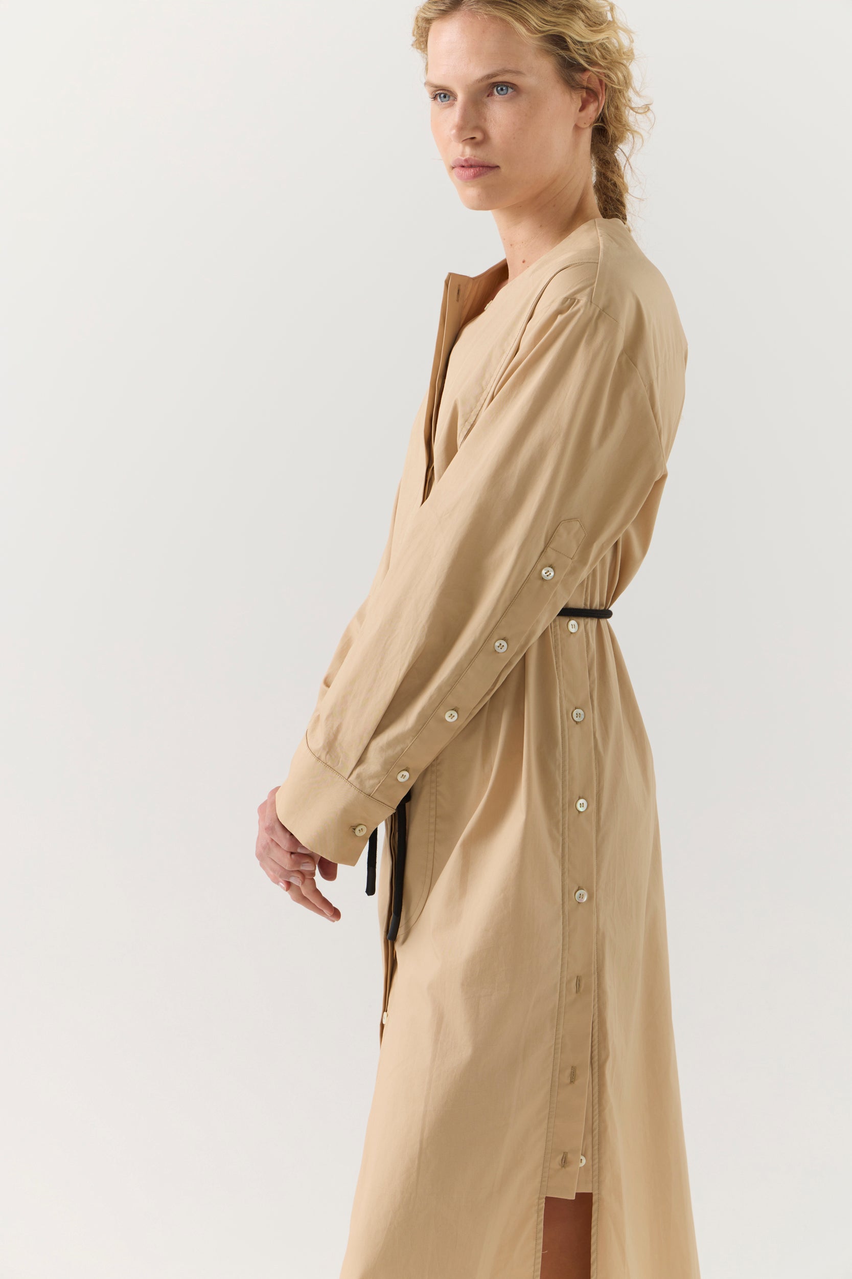 Woman wearing a beige dress with a belt on a white background