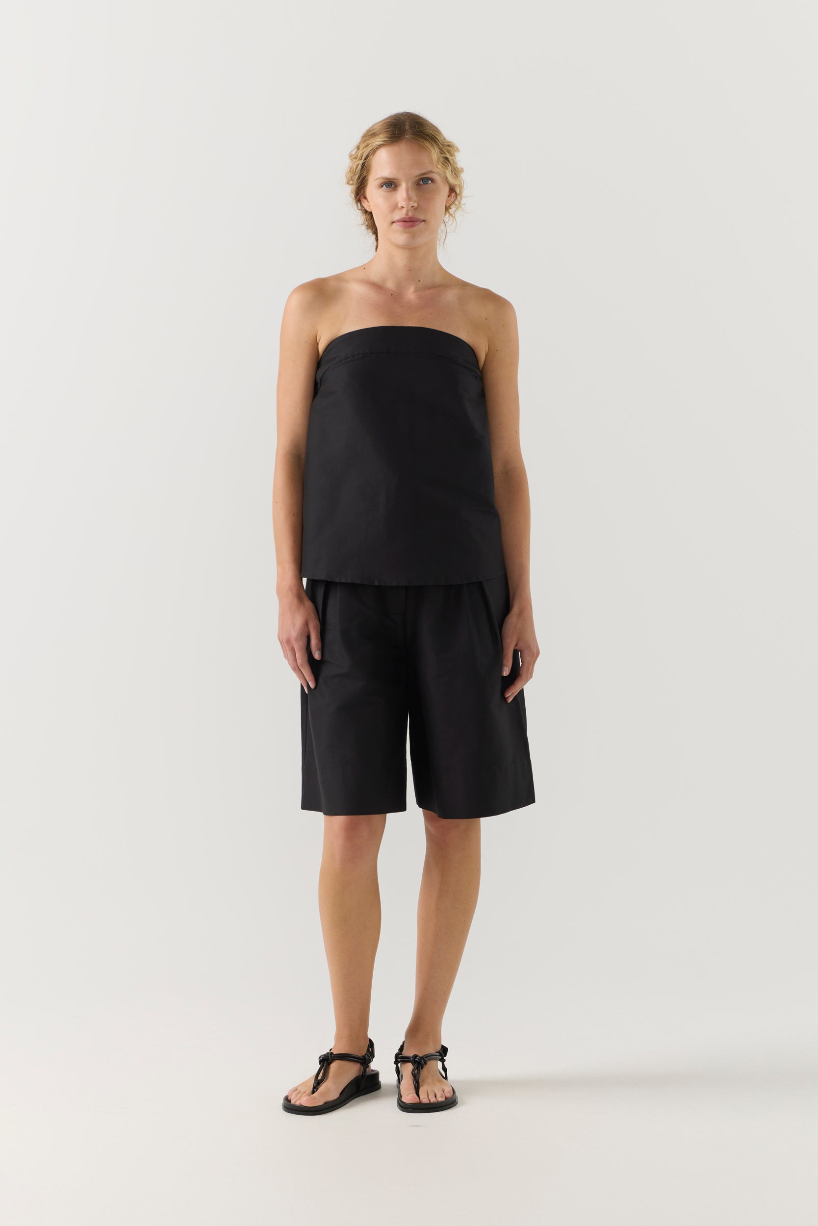 Woman wearing a black strapless top and black shorts on a white background