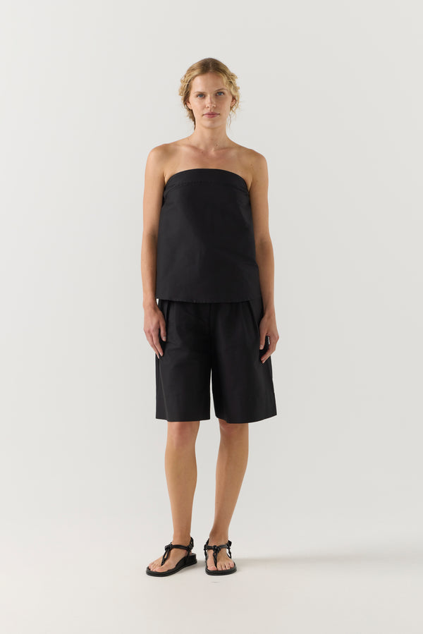 Woman wearing a black strapless top and black shorts on a white background