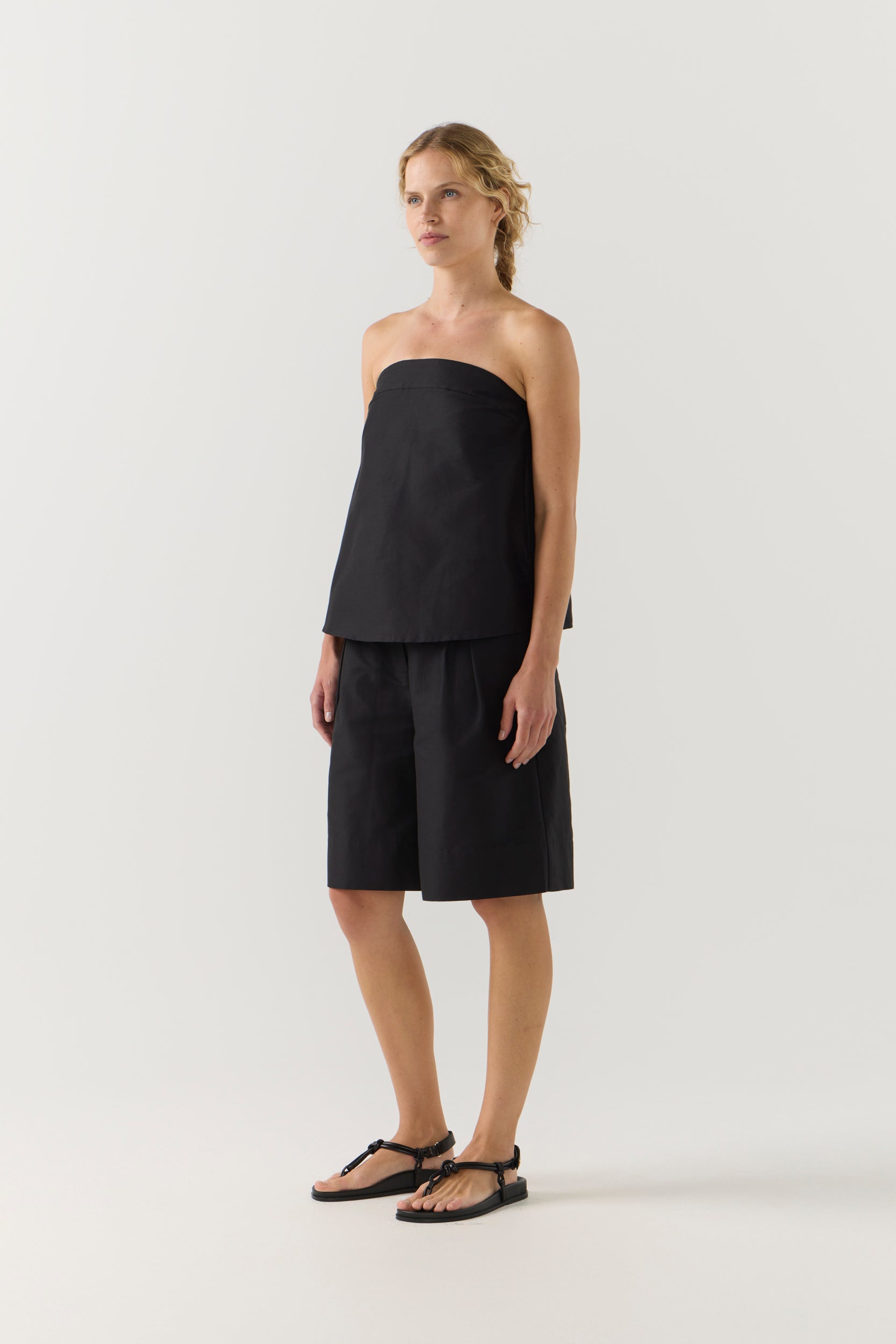 Woman wearing a black strapless top and black shorts on a white background