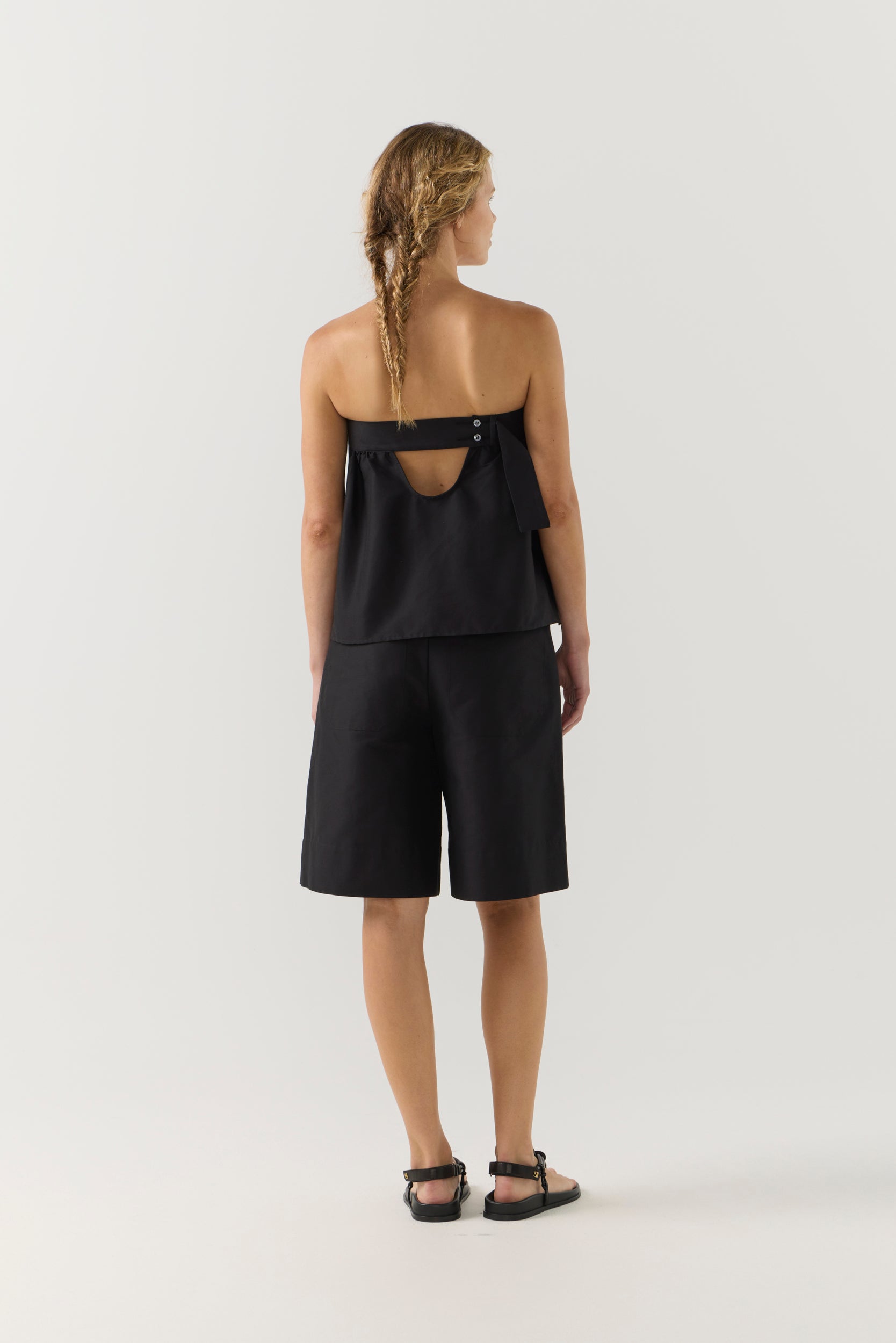 Woman wearing a black strapless top and black shorts on a white background