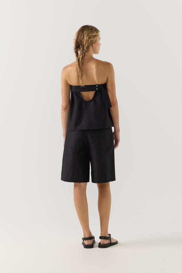 Woman wearing a black strapless top and black shorts on a white background