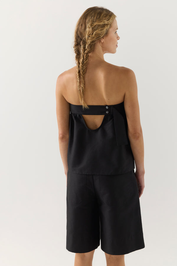 Woman wearing a black strapless top and black shorts on a white background