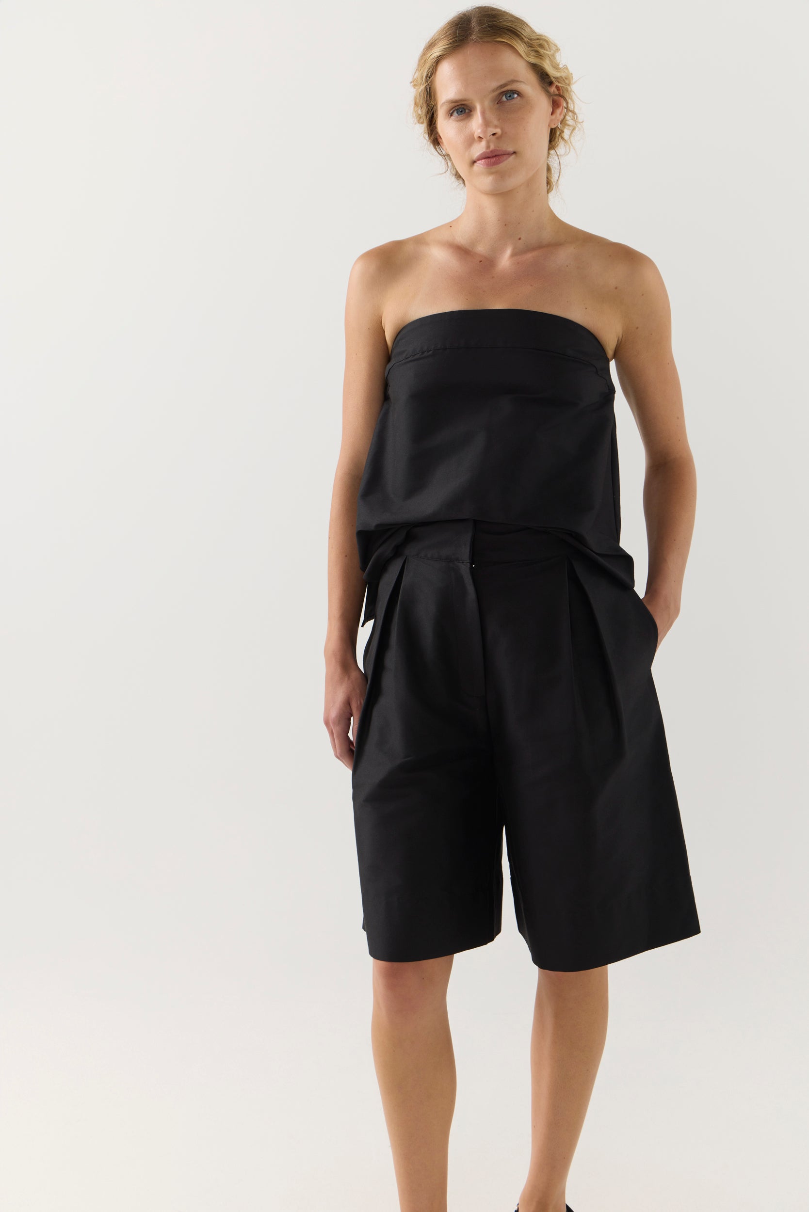 Woman wearing a black strapless top and black shorts on a white background