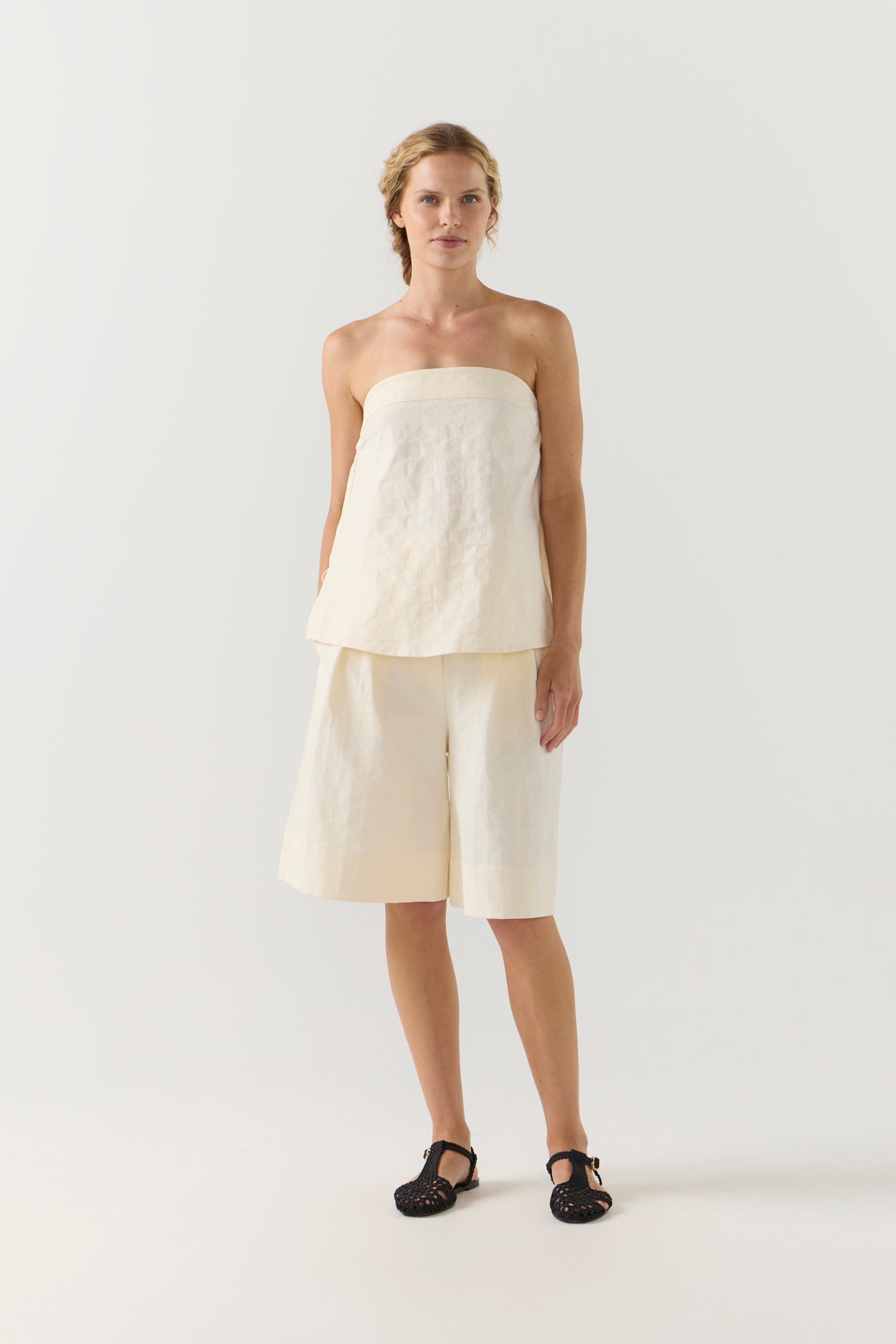 Woman wearing a strapless white top and shorts on a white background