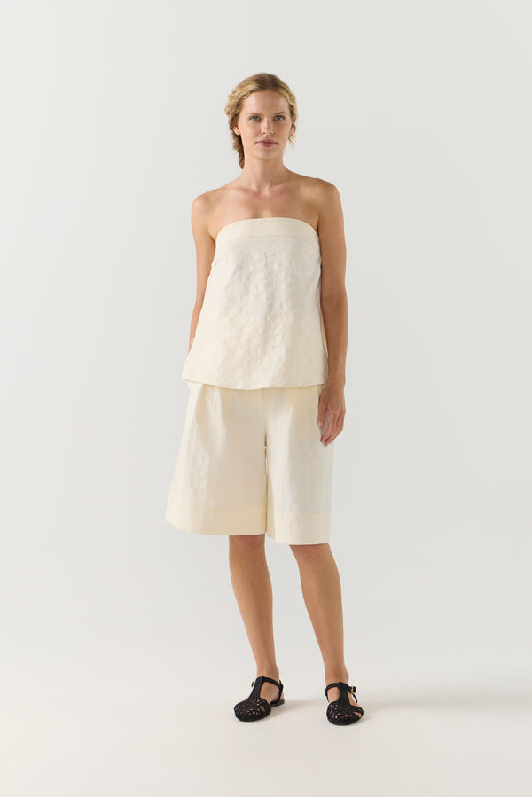 Woman wearing a strapless white top and shorts on a white background
