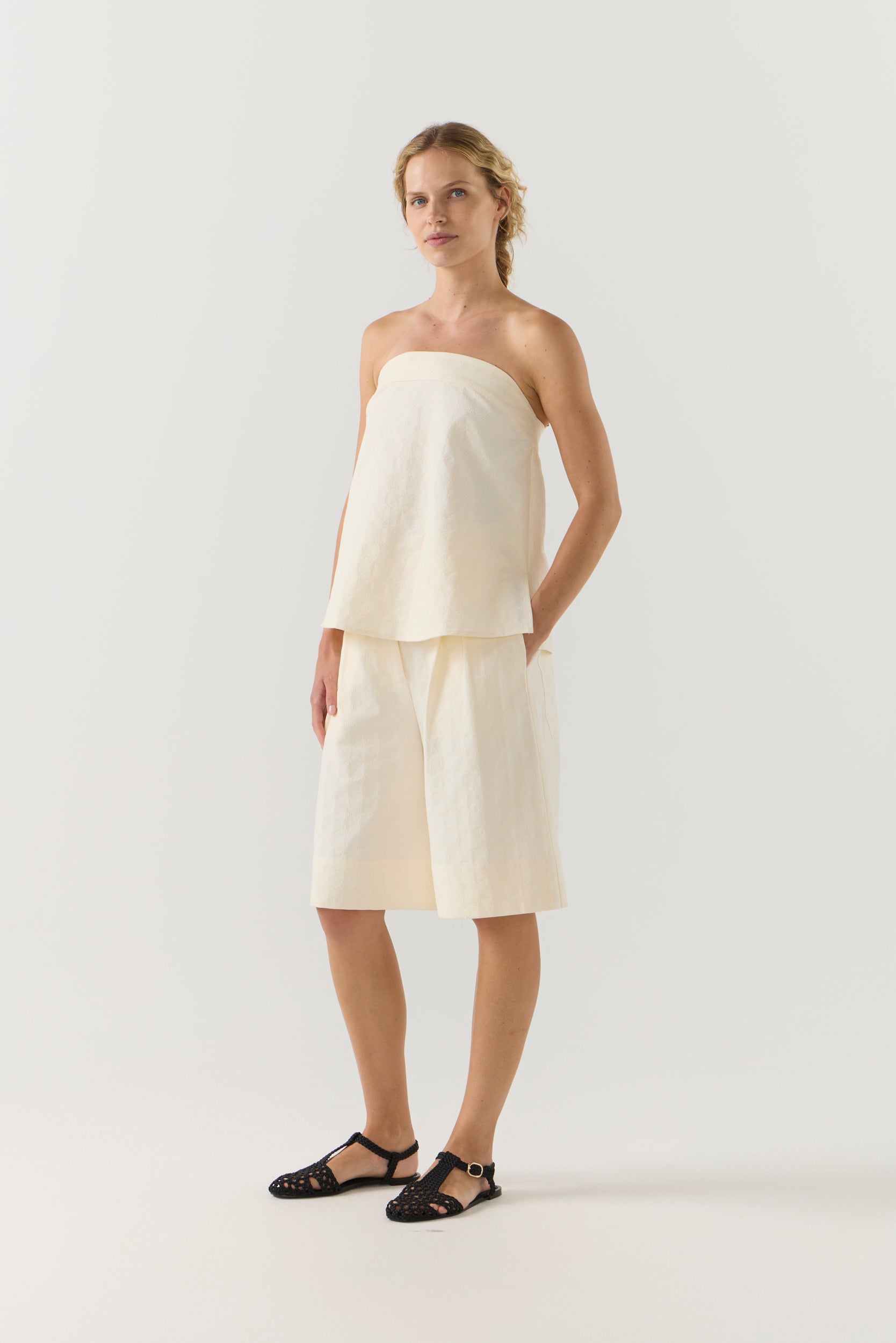 Woman wearing a strapless white top and shorts on a white background
