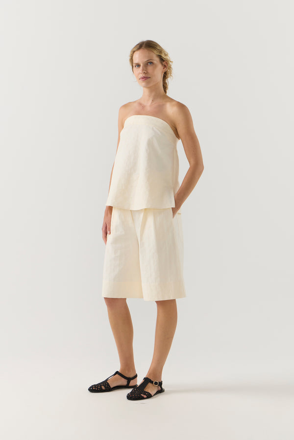 Woman wearing a strapless white top and shorts on a white background