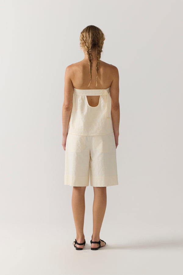 Woman wearing a strapless white top and shorts on a white background