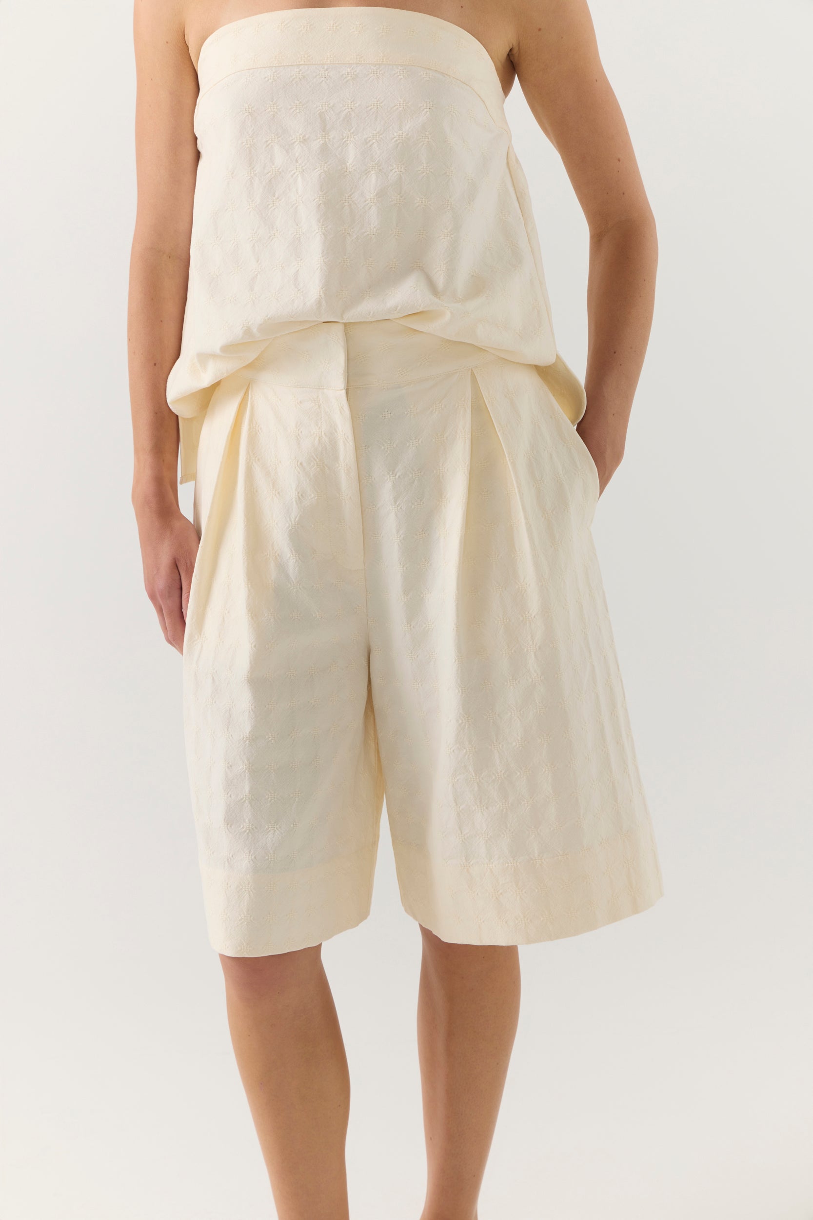Woman wearing a strapless white top and shorts on a white background