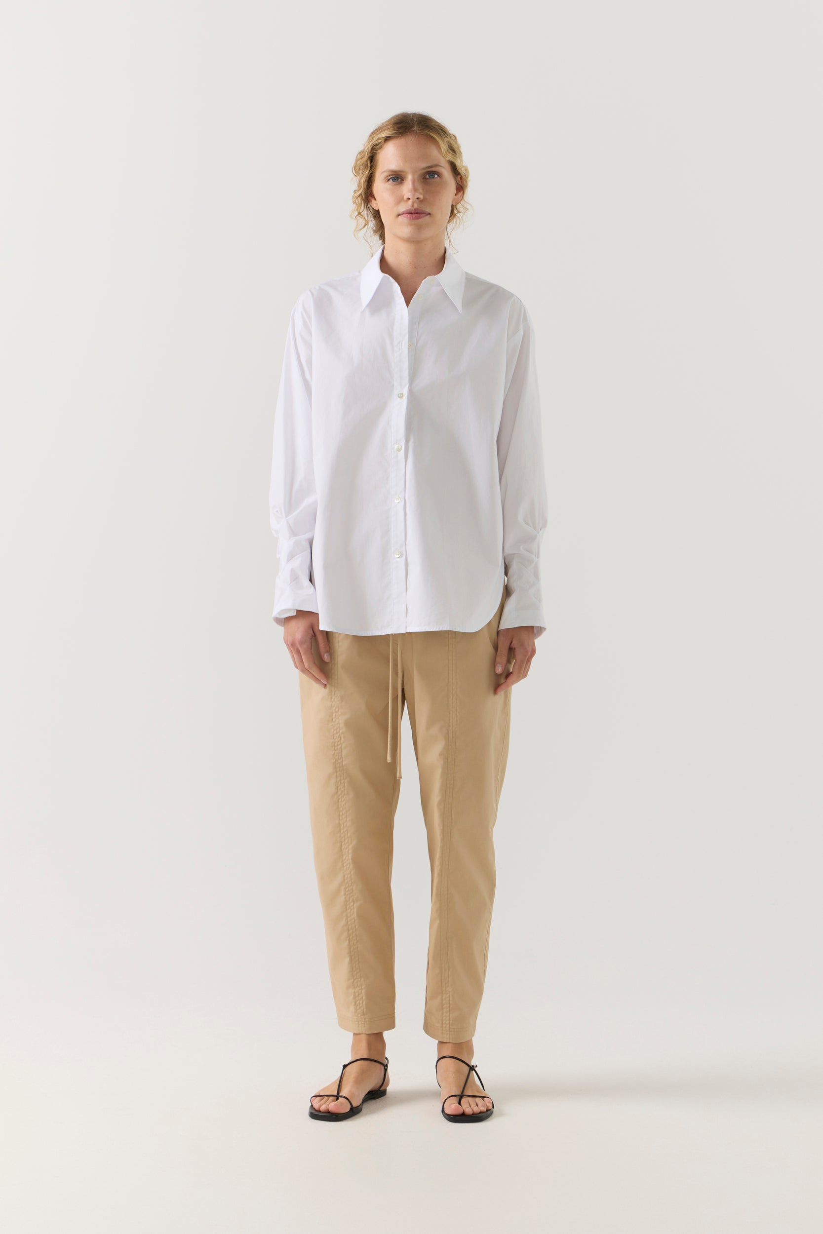 Person wearing a white shirt and beige pants on a white background