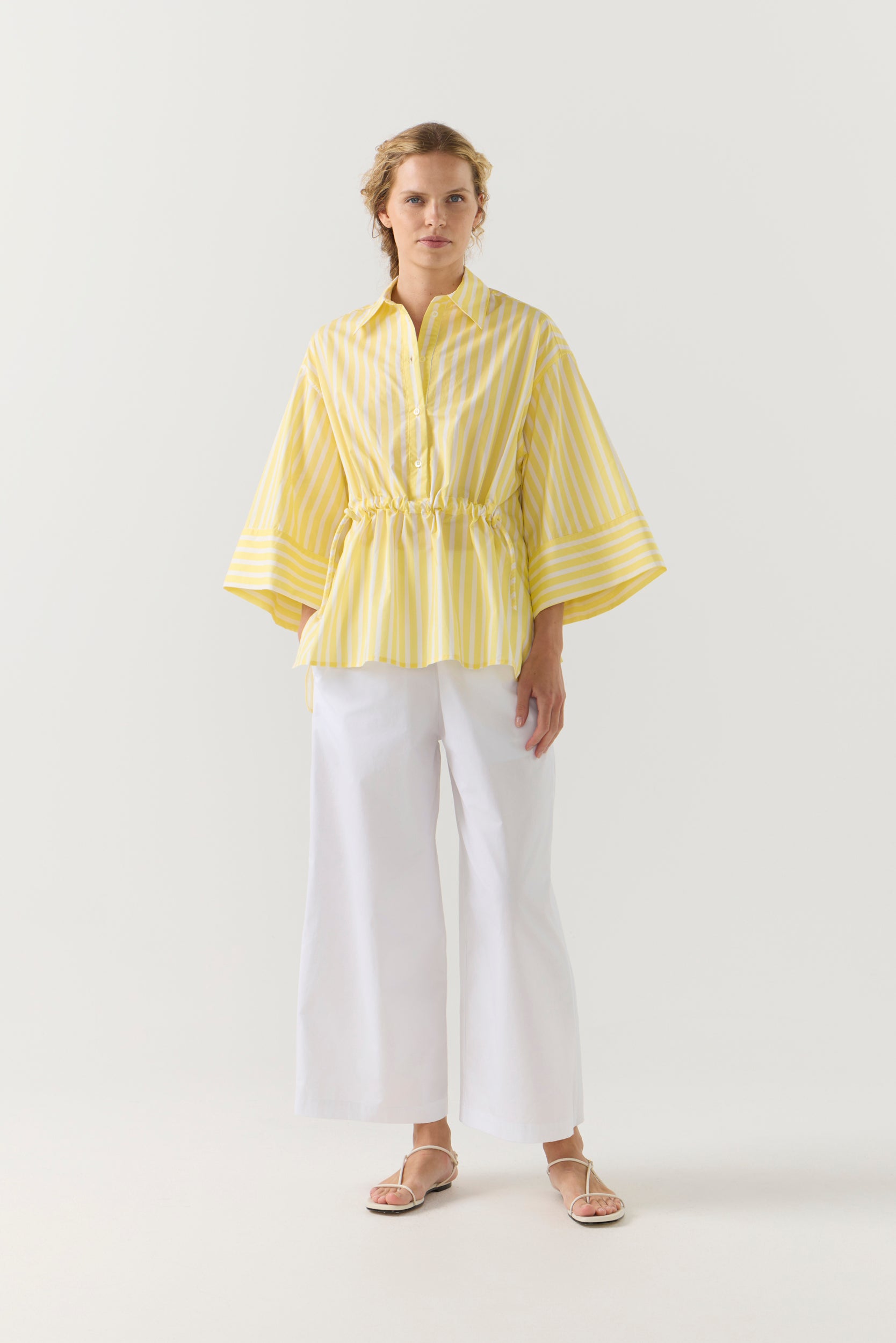 Woman wearing a yellow striped shirt and white pants on a white background