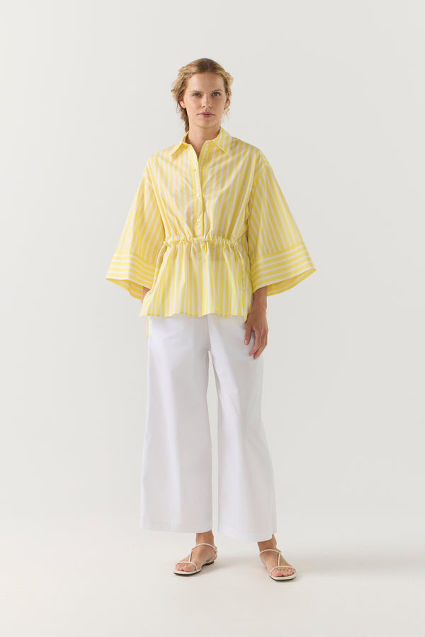 Woman wearing a yellow striped shirt and white pants on a white background