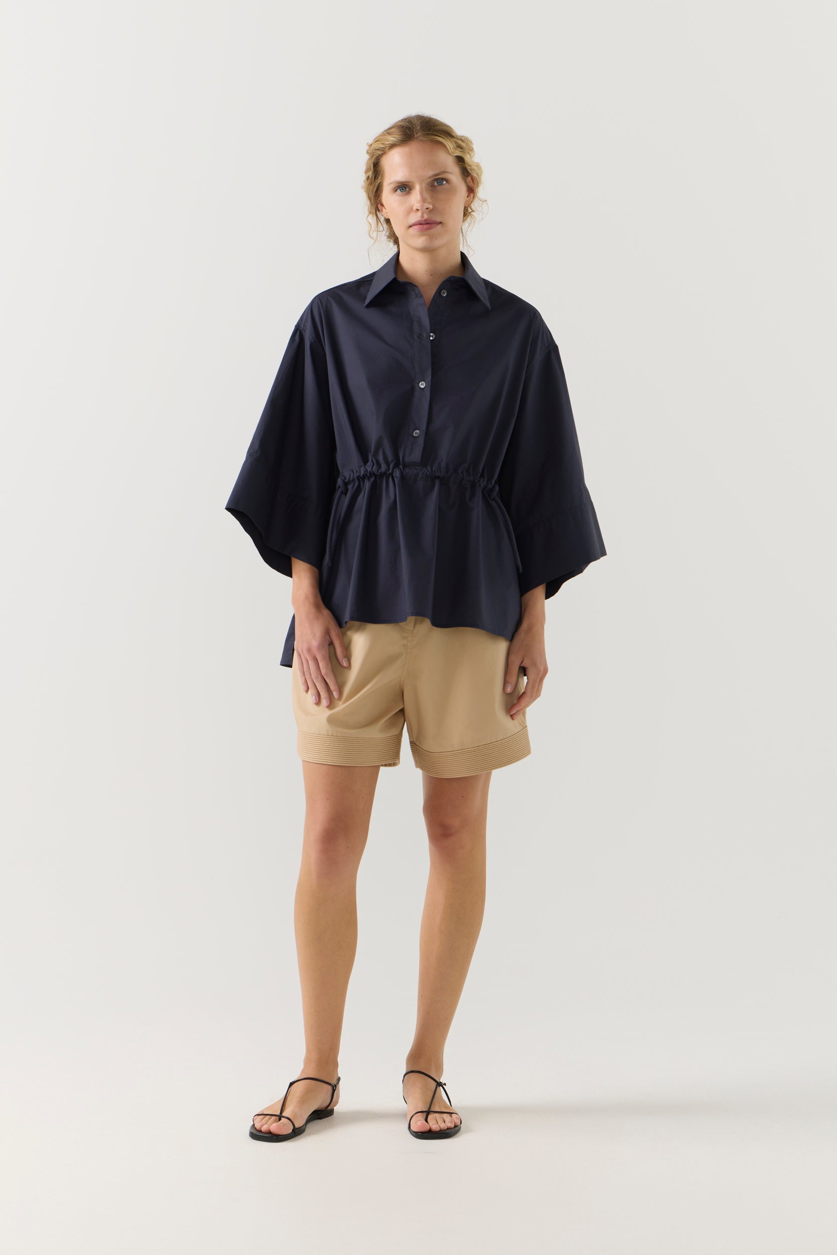 Woman wearing a navy blue blouse and beige shorts on a white background