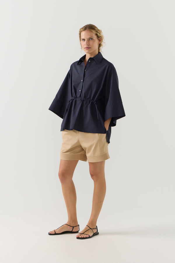 Woman wearing a navy blue blouse and beige shorts on a white background