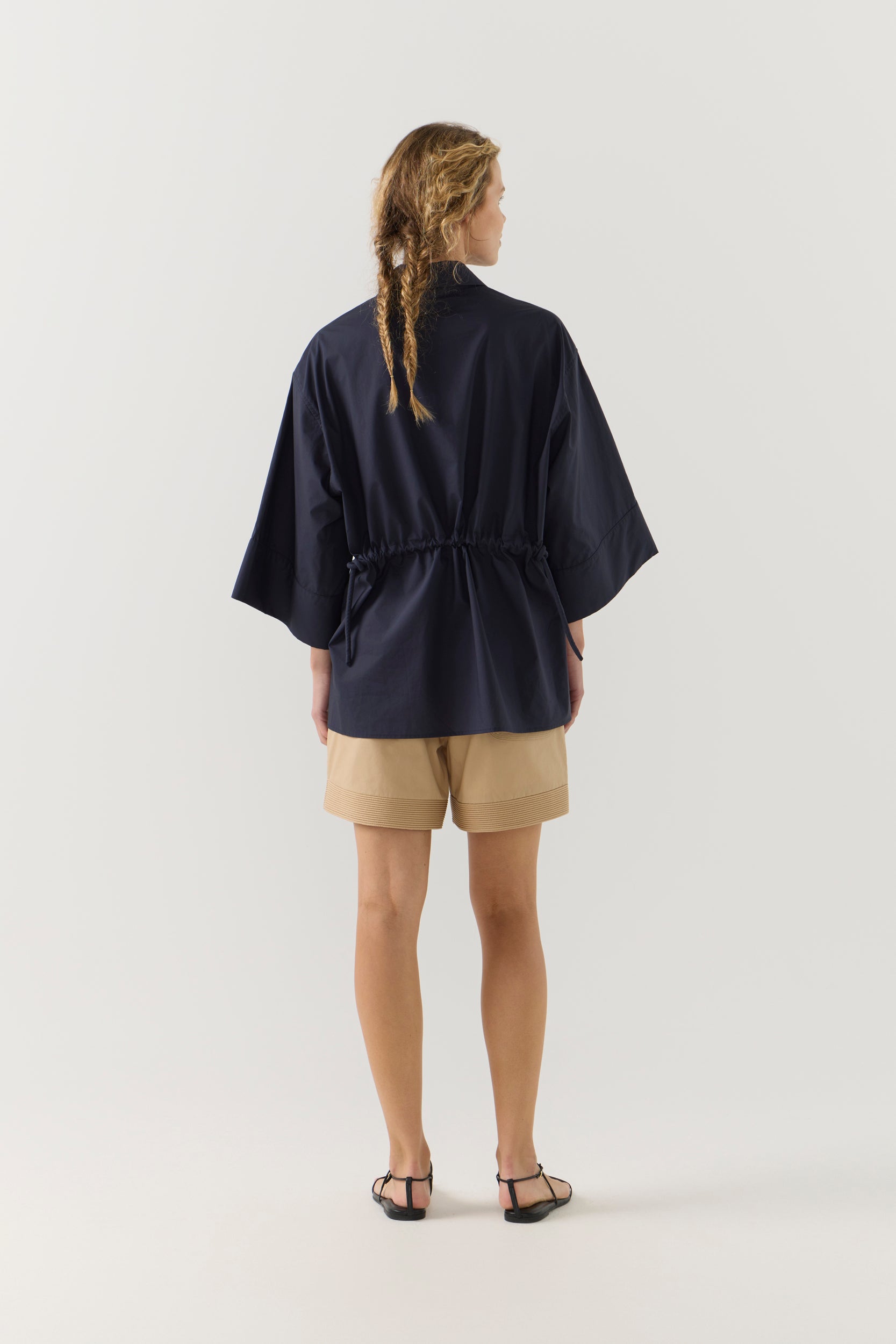 Woman wearing a navy blue blouse and beige shorts on a white background