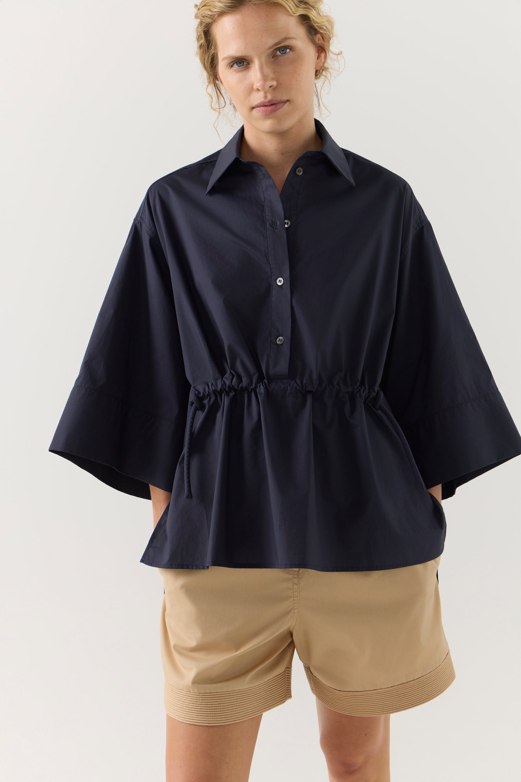 Woman wearing a navy blue blouse and beige shorts on a white background