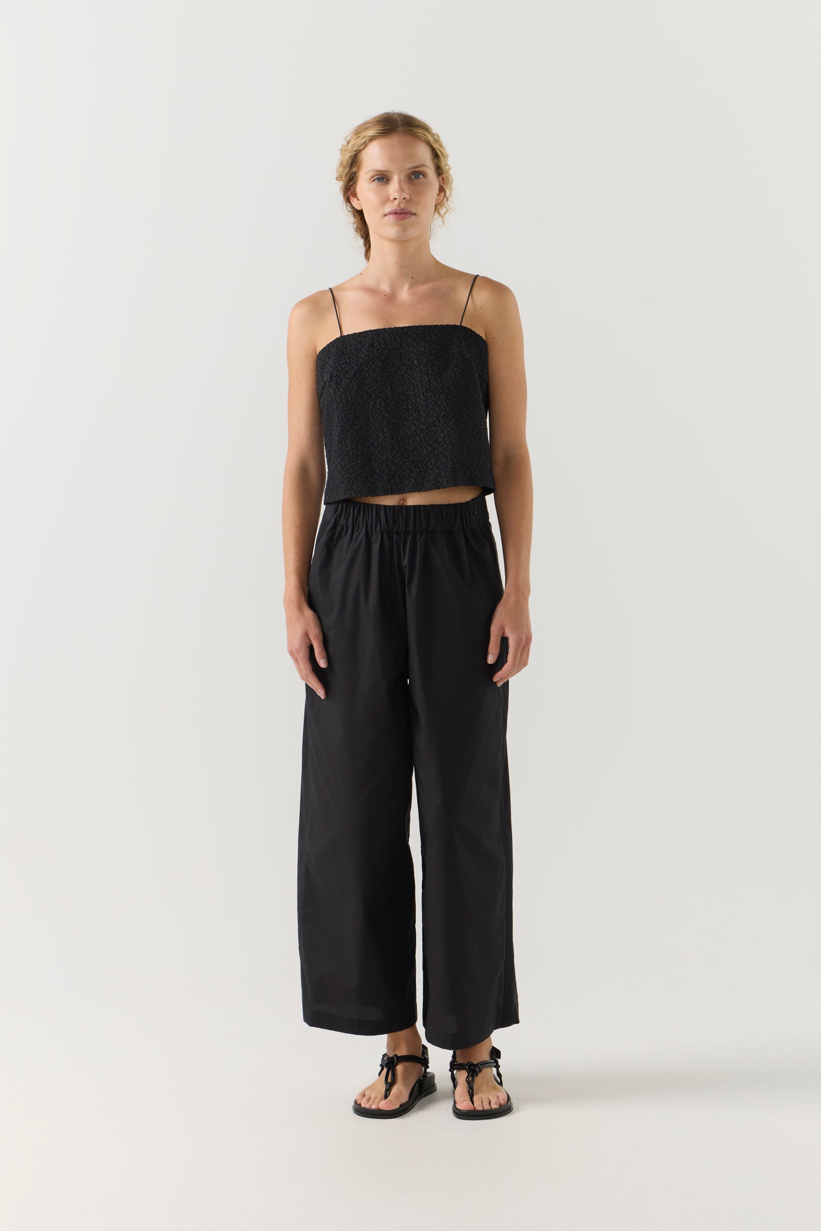Woman wearing a black strap top and wide-leg pants on a white background