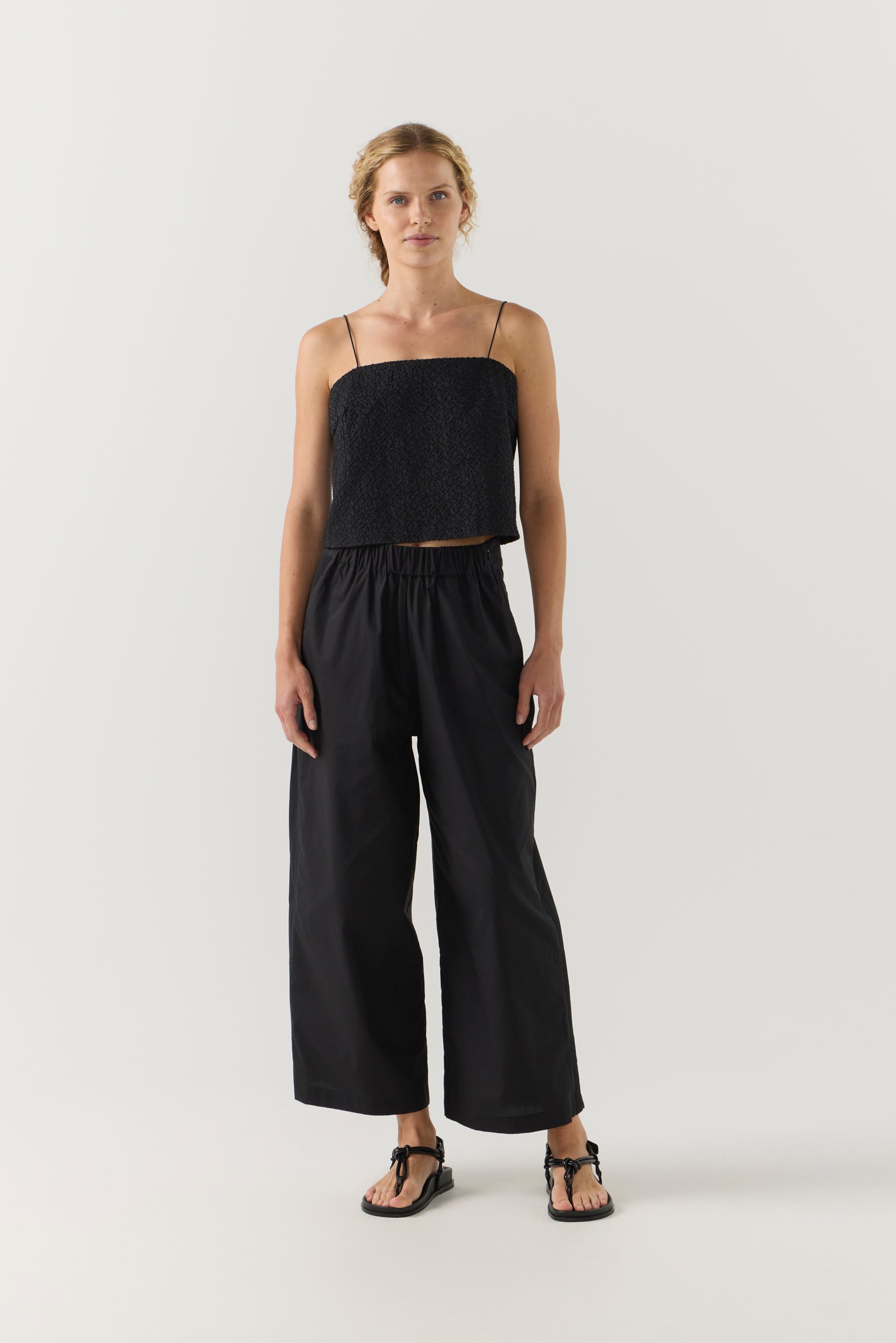 Woman wearing a black strap top and wide-leg pants on a white background