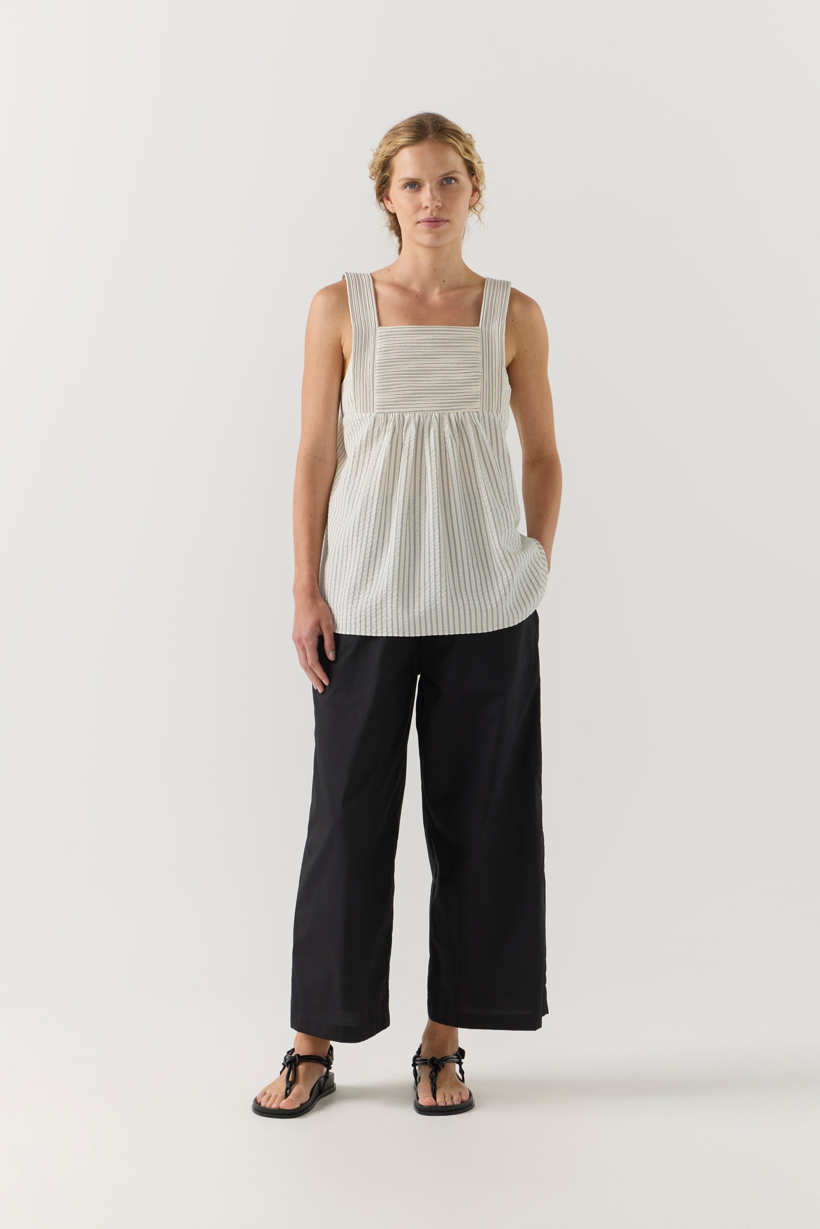 Woman wearing a sleeveless, striped top with a plain background