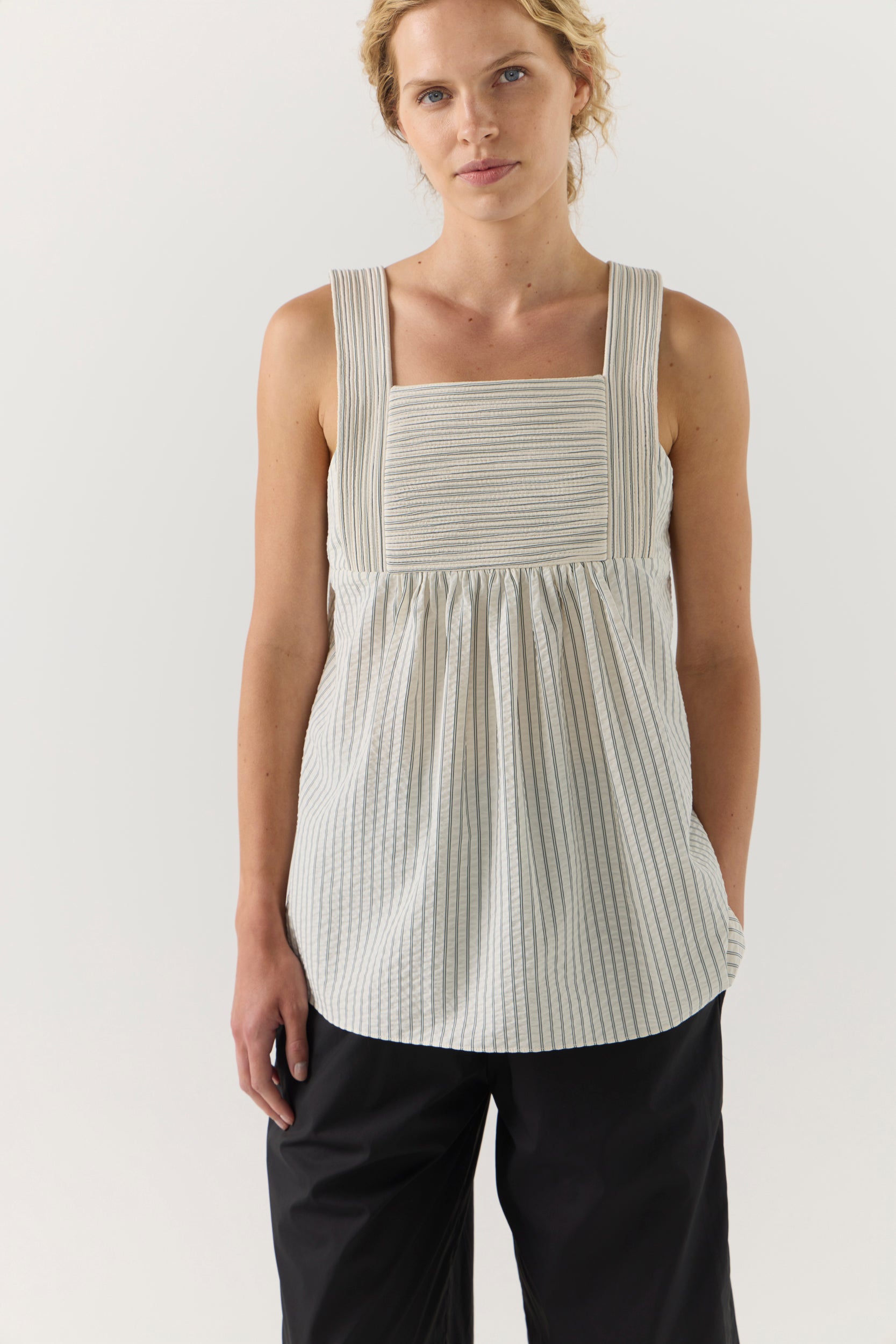 Woman wearing a sleeveless, striped top with a plain background