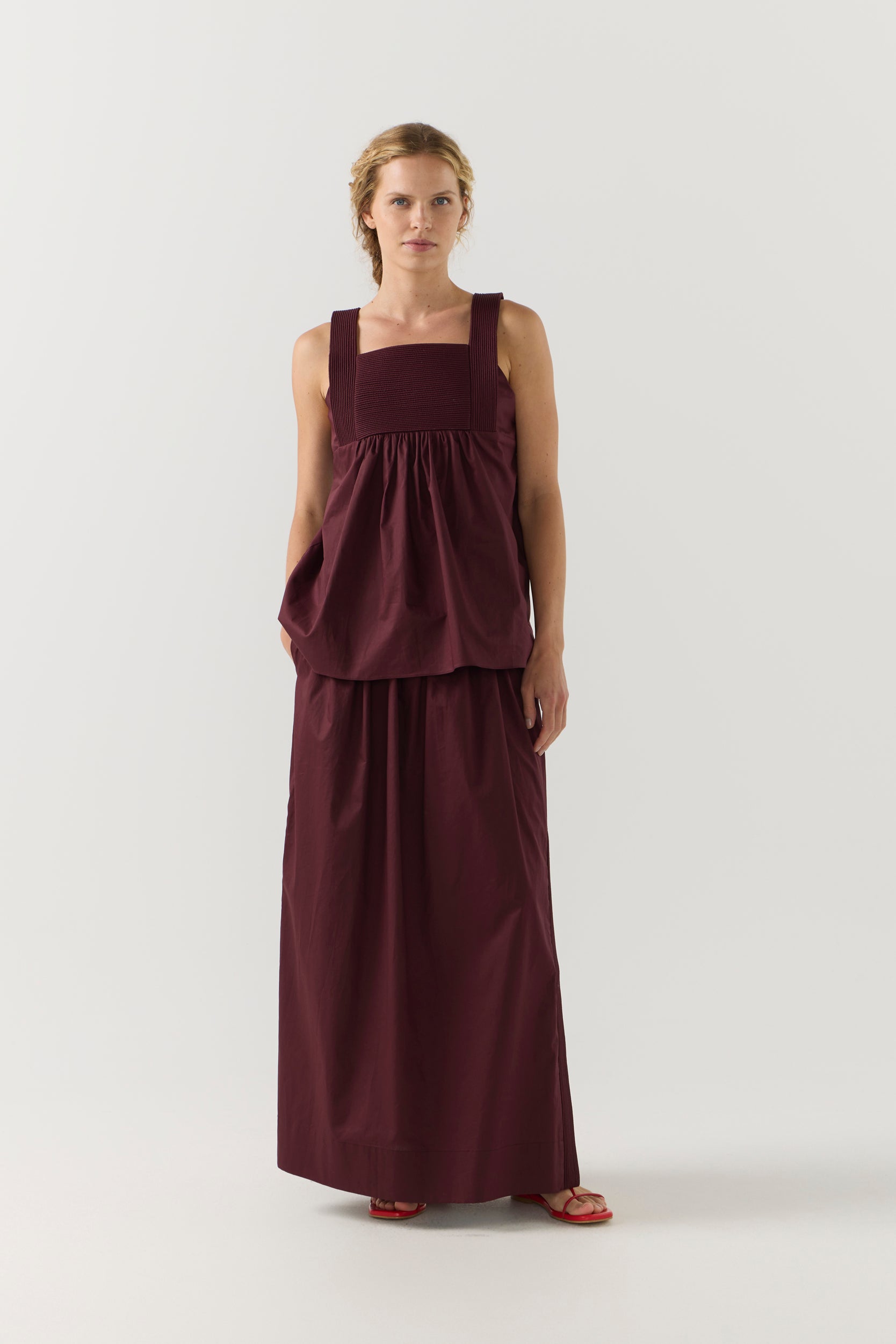 Woman wearing a burgundy sleeveless top and long skirt on a white background