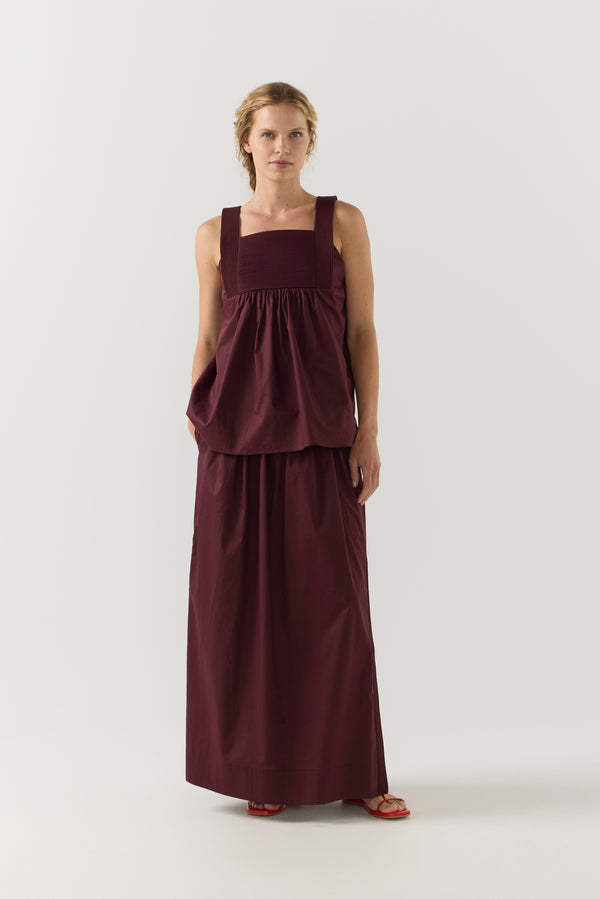 Woman wearing a burgundy sleeveless top and long skirt on a white background