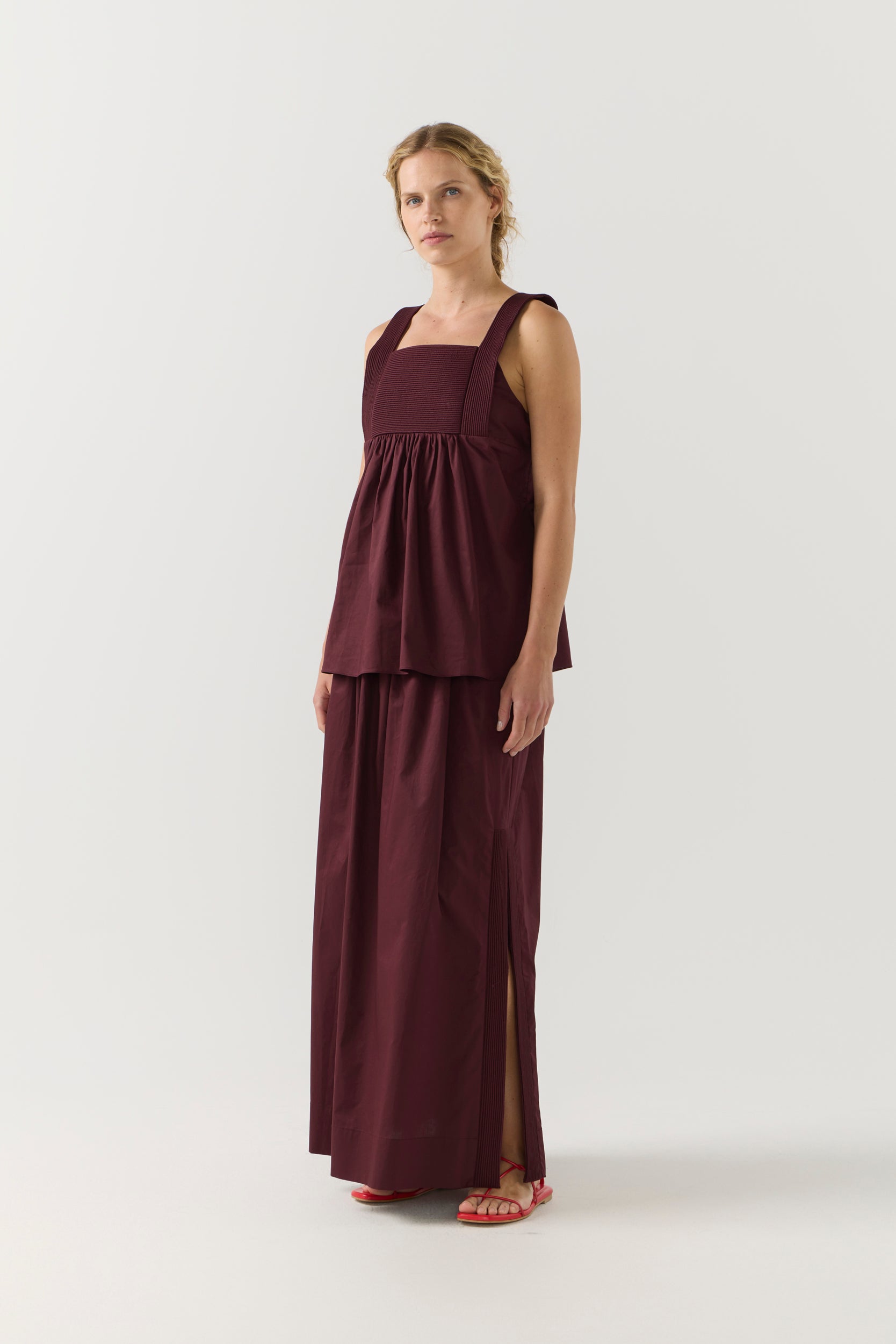 Woman wearing a burgundy sleeveless top and long skirt on a white background
