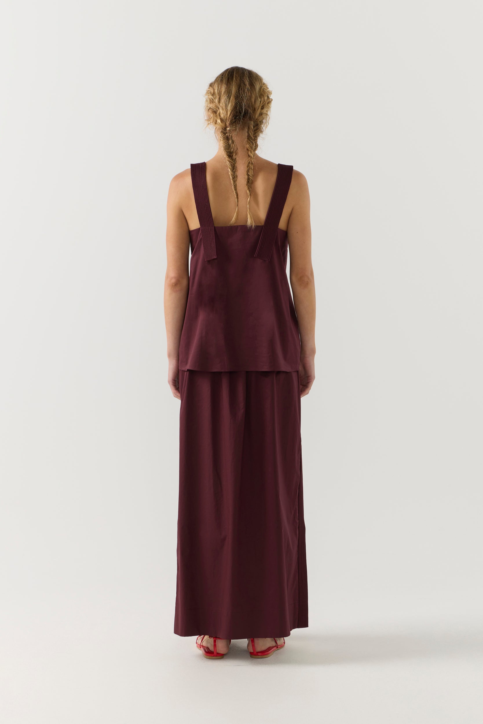 Woman wearing a burgundy sleeveless top and long skirt on a white background