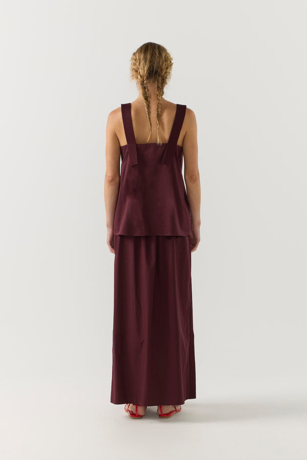 Woman wearing a burgundy sleeveless top and long skirt on a white background