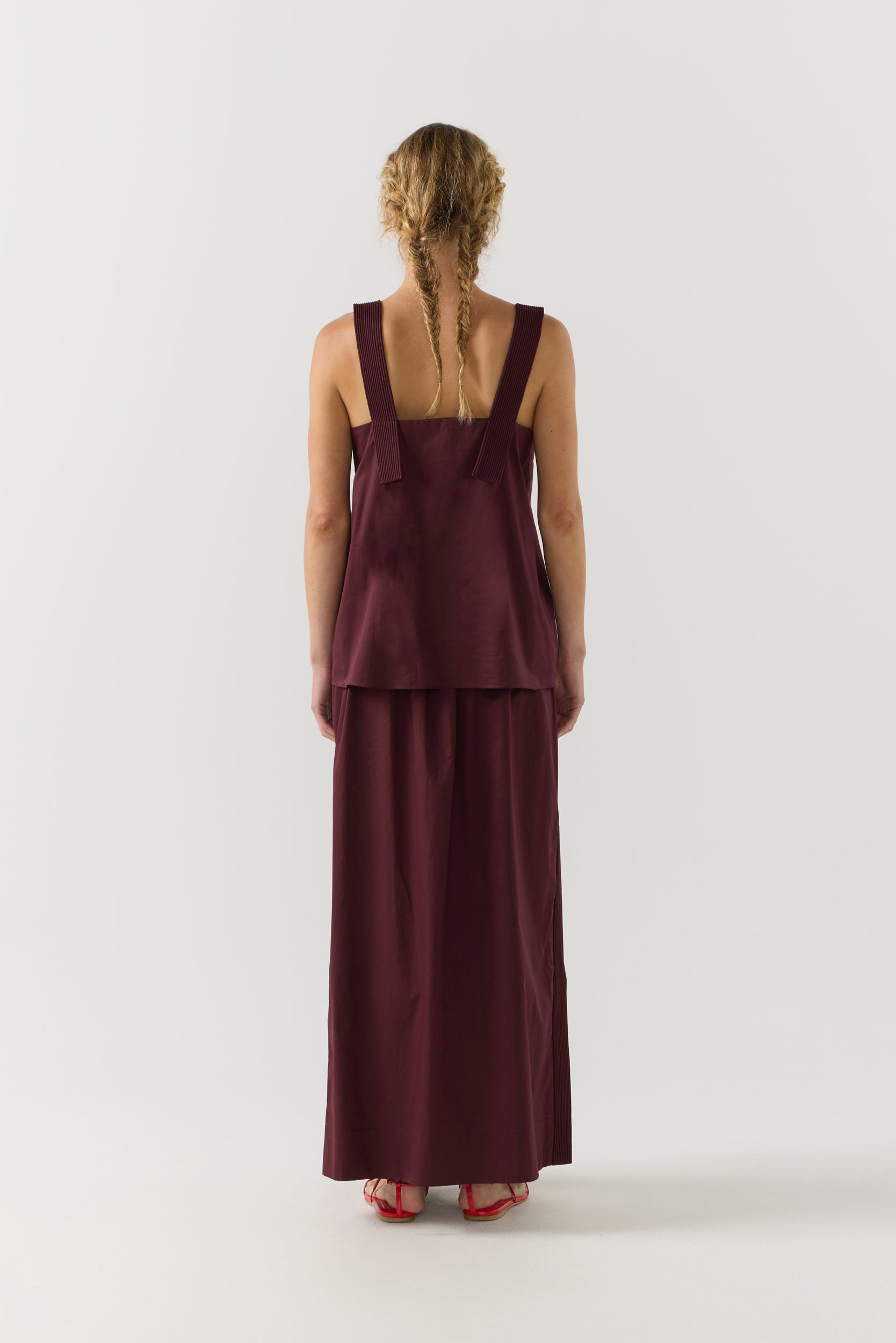 Woman wearing a burgundy sleeveless top and long skirt on a white background