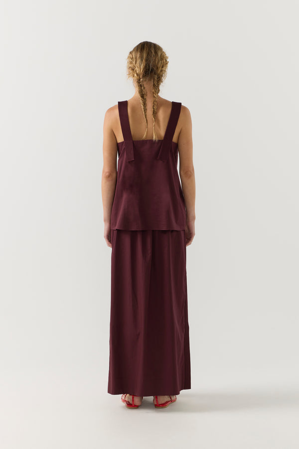 Woman wearing a burgundy sleeveless top and long skirt on a white background