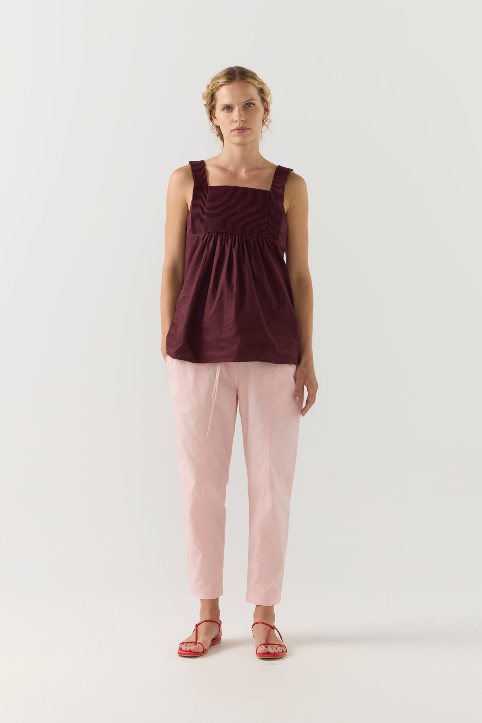 Woman wearing a burgundy sleeveless top and light pink pants on a white background