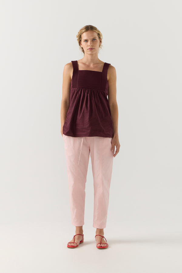 Woman wearing a burgundy sleeveless top and light pink pants on a white background