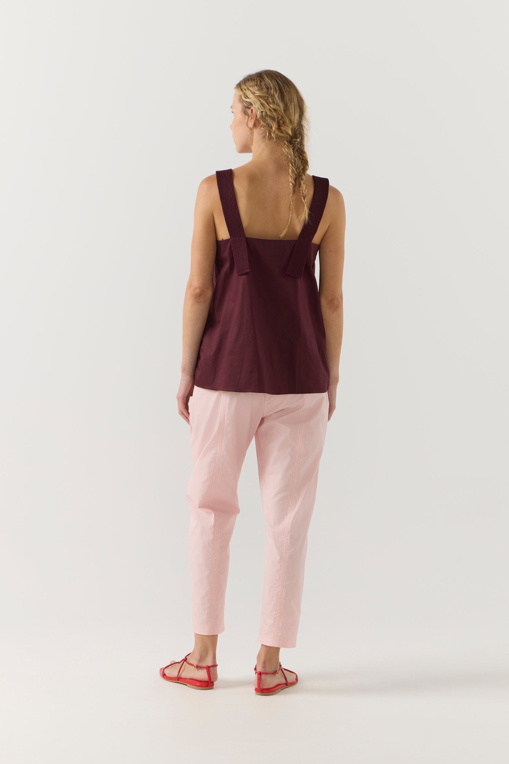 Woman wearing a burgundy sleeveless top and light pink pants on a white background