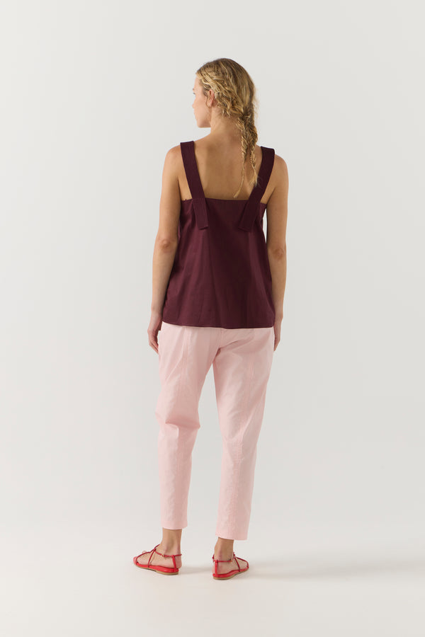 Woman wearing a burgundy sleeveless top and light pink pants on a white background