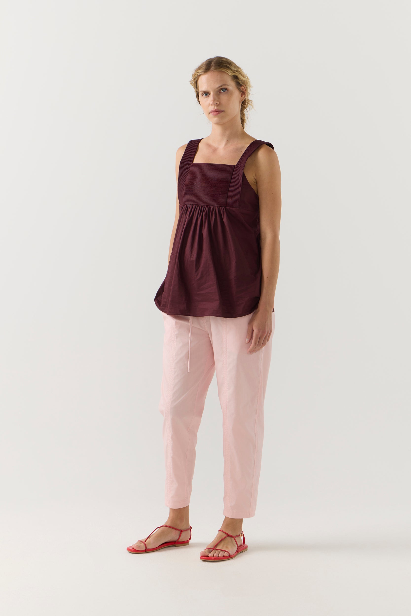 Woman wearing a burgundy sleeveless top and light pink pants on a white background