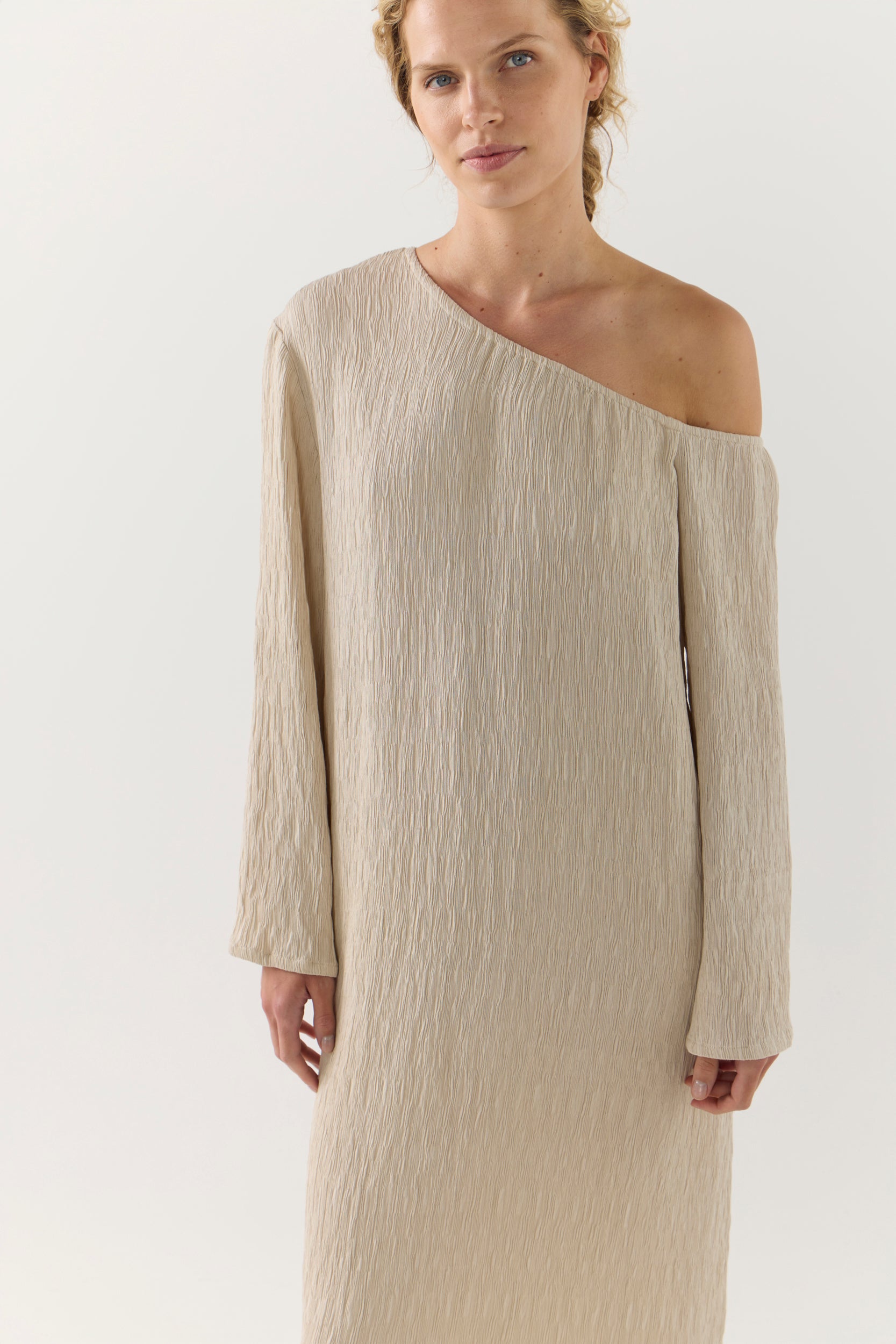 Woman wearing a beige one-shoulder dress on a white background