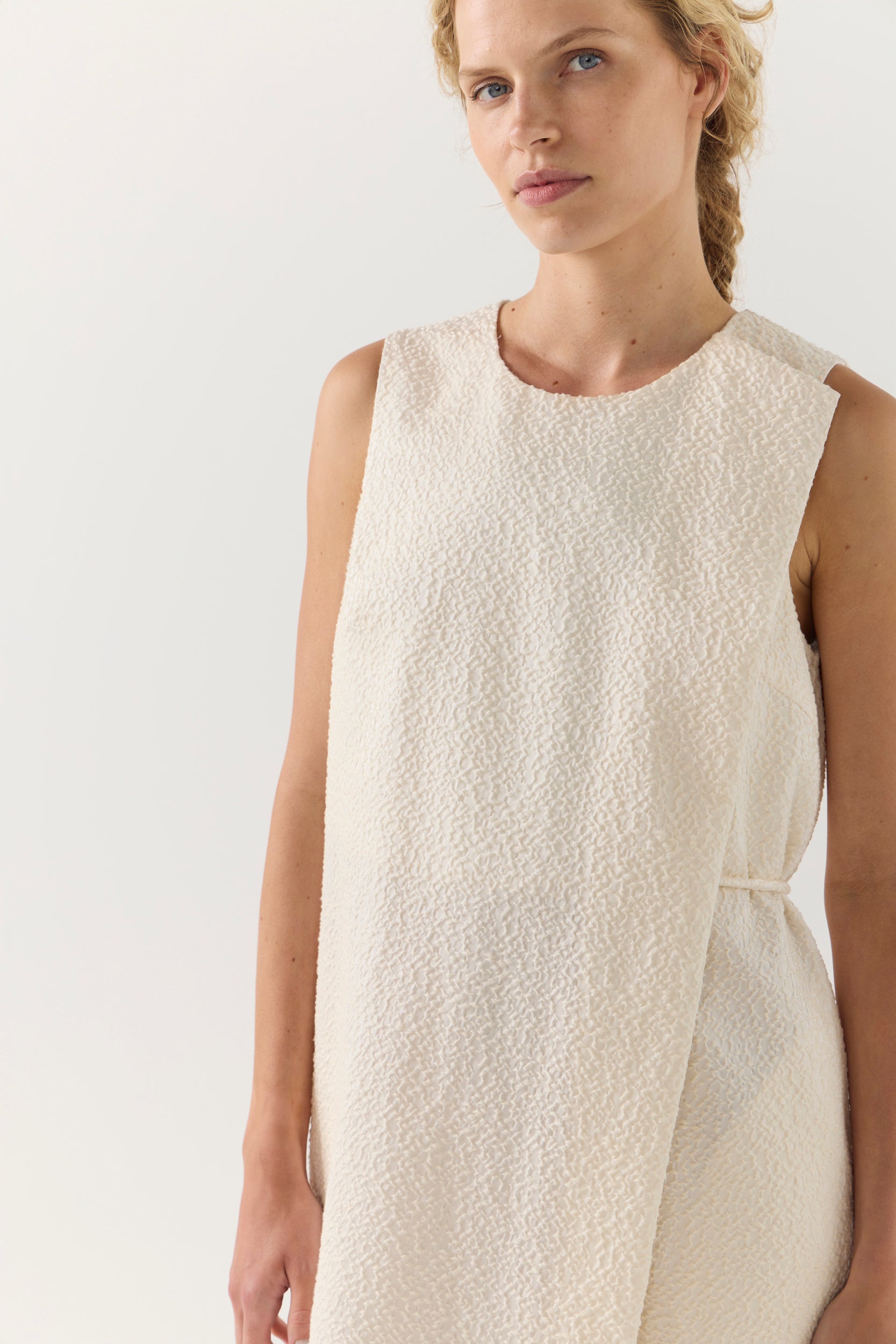 Woman wearing a beige sleeveless dress against a plain background