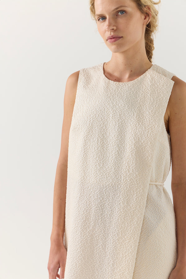 Woman wearing a beige sleeveless dress against a plain background