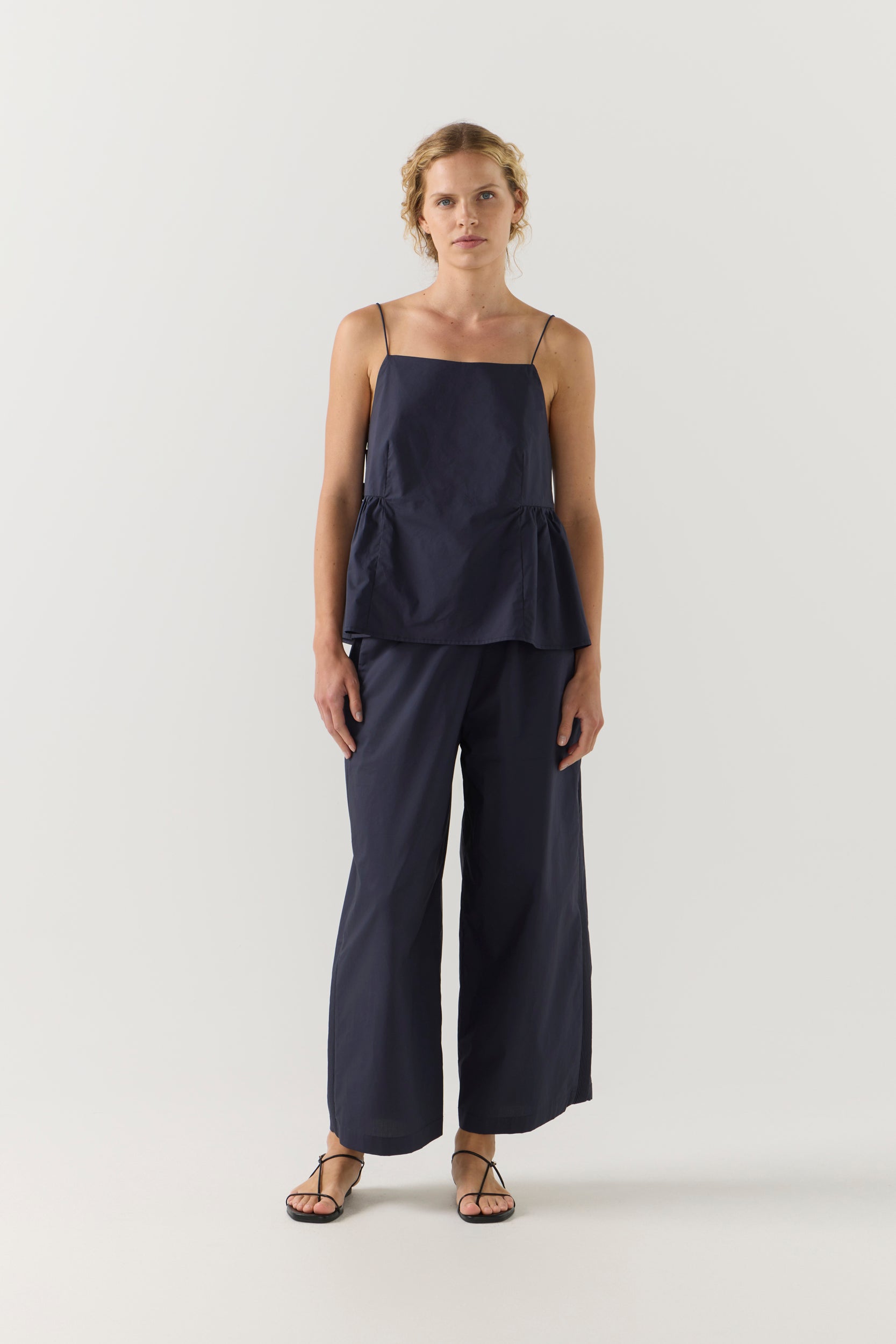 Woman wearing a navy blue singlet and pant on a white background