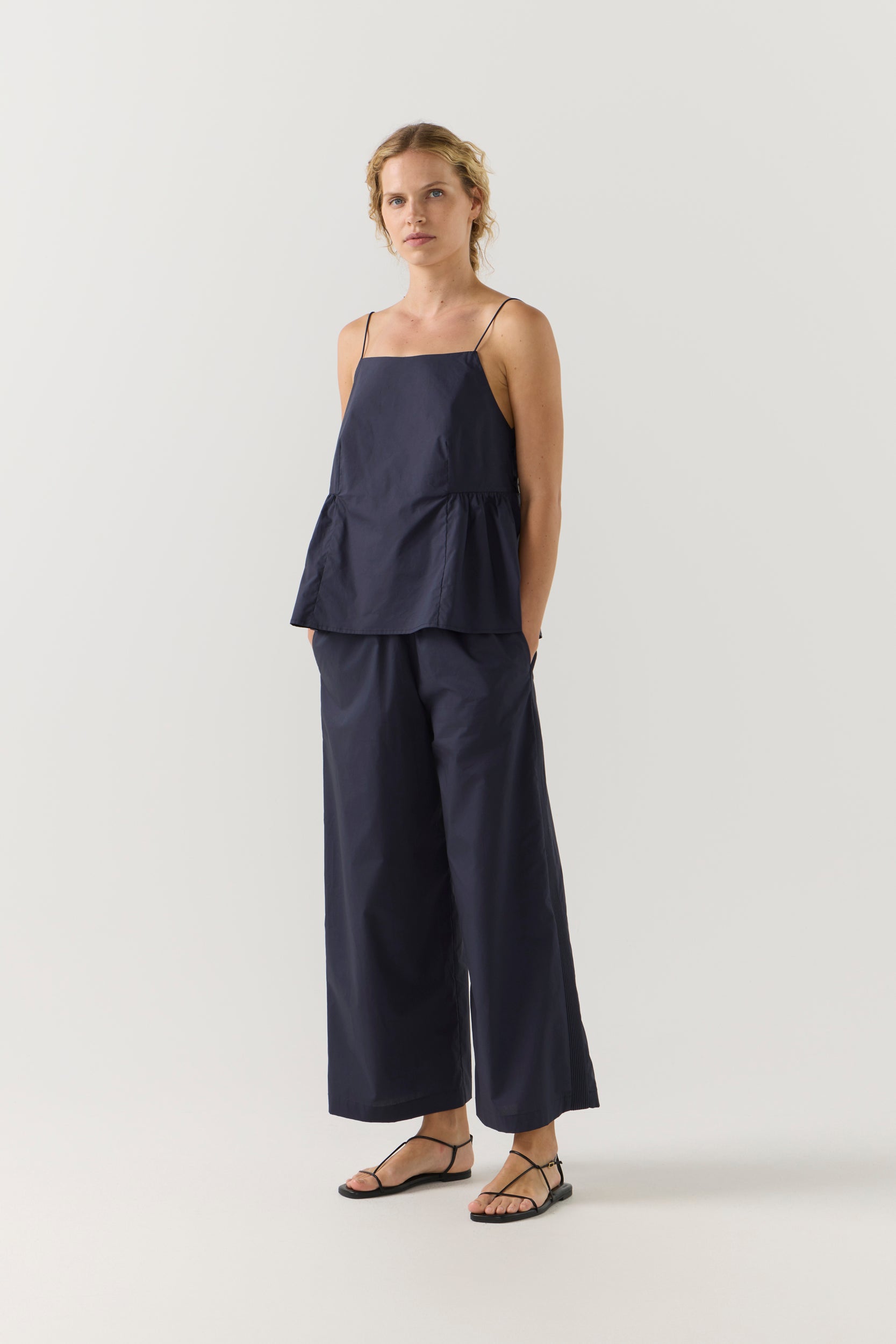 Woman wearing a navy blue singlet and pant on a white background